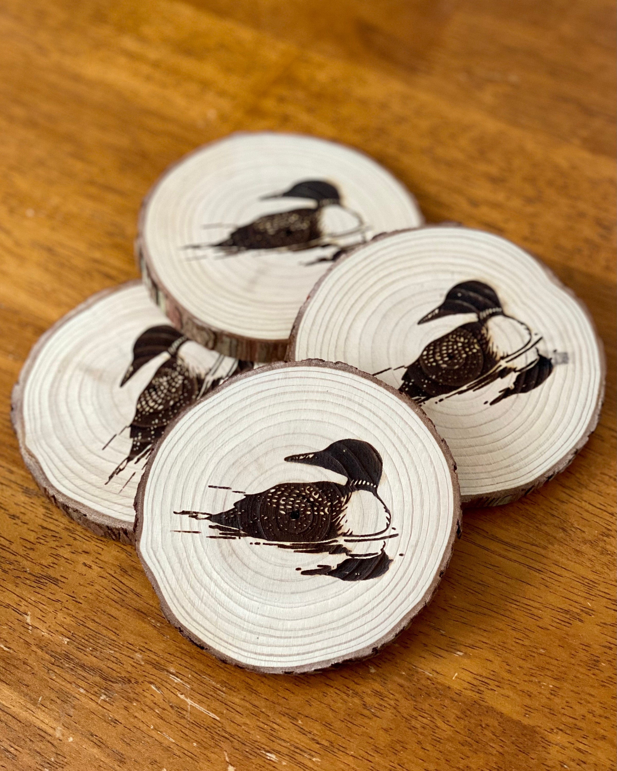 A set of four laser engraved wood coasters featuring a detailed loon illustration, showcasing their natural wood finish and rustic charm.