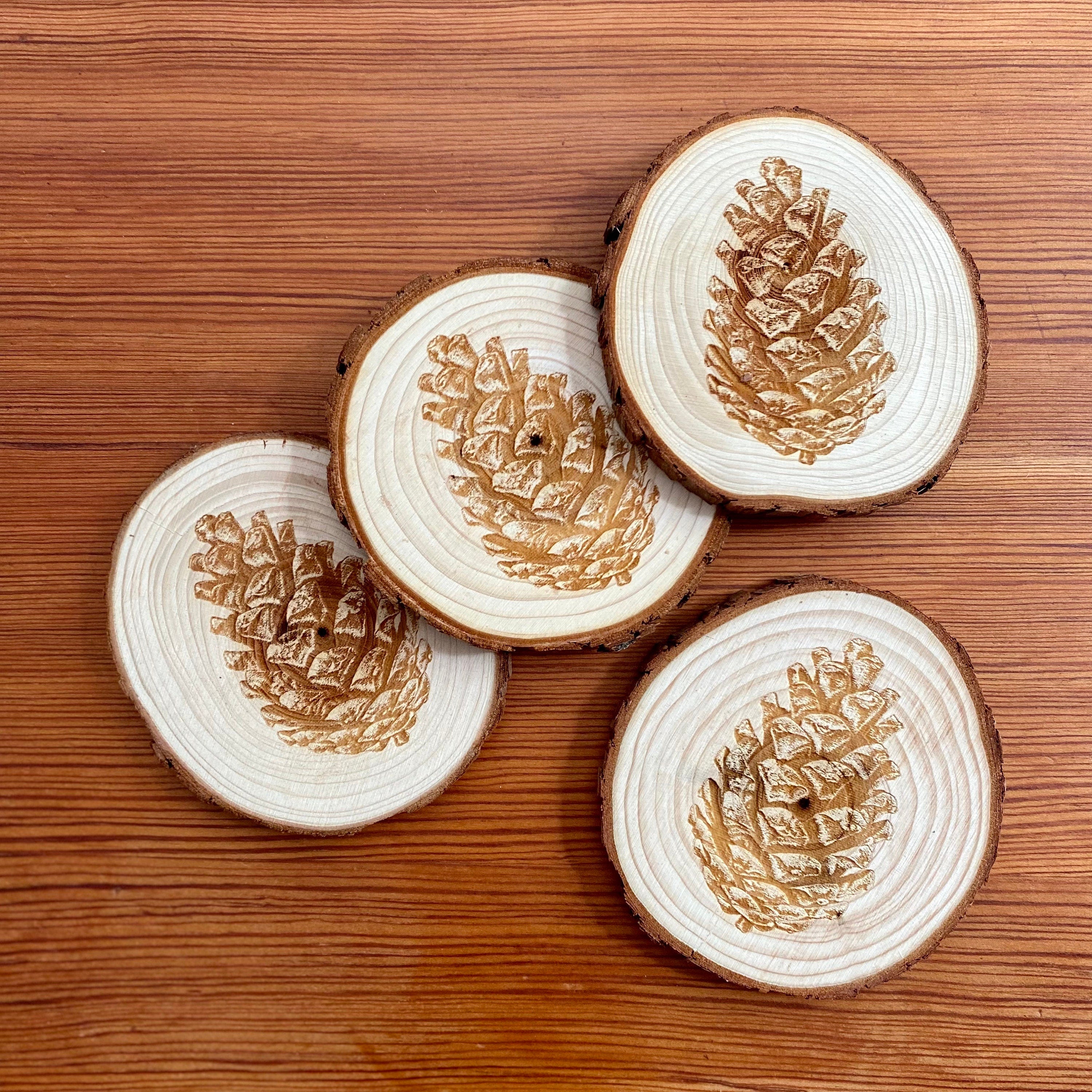 A set of four pine cone engraved wood coasters, showcasing intricate designs on a natural wood surface, ideal for home decor.