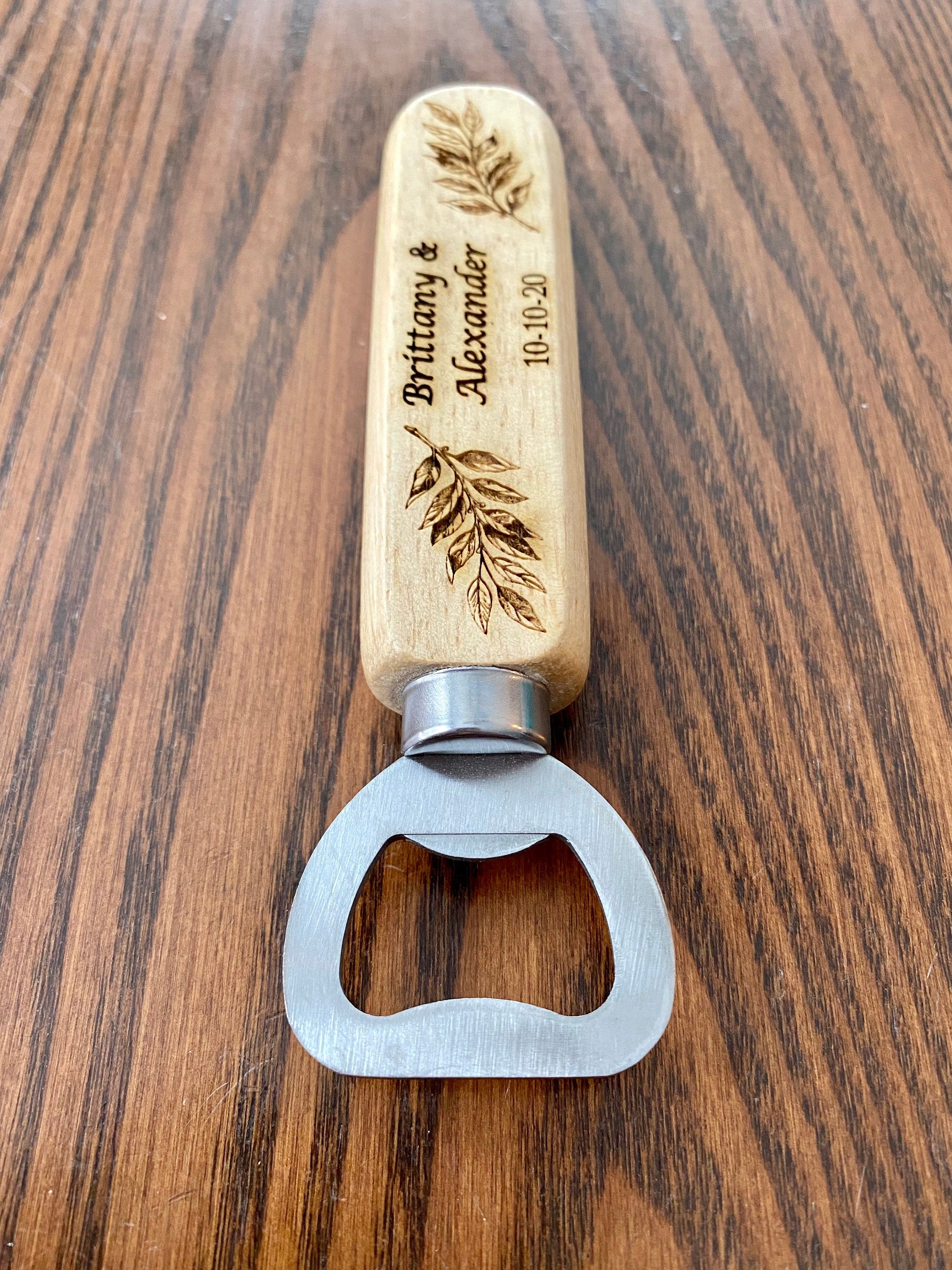 Personalized wooden bottle opener with engraved names and leaf design, perfect for rustic wedding favors.