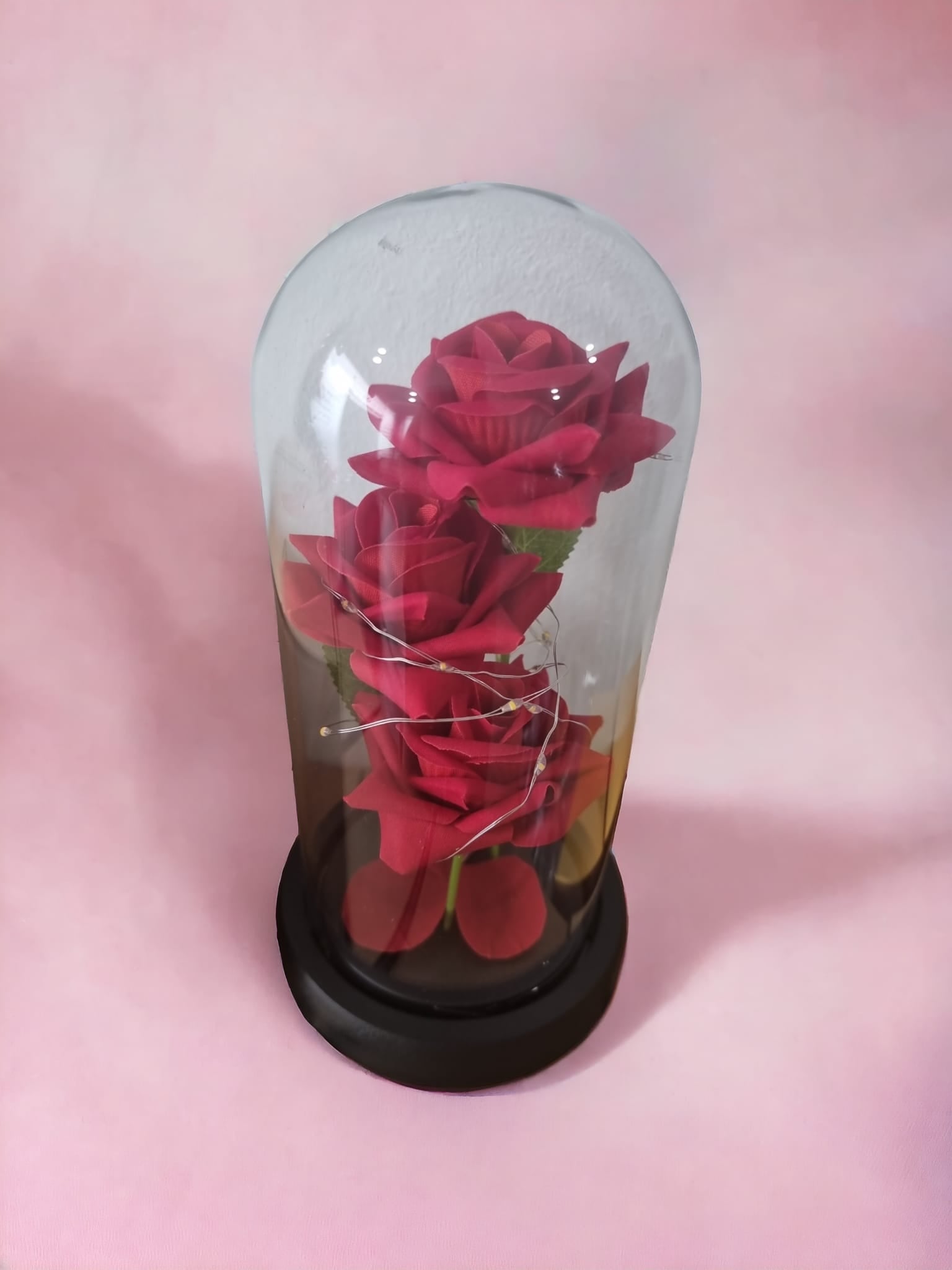 Three red roses beautifully arranged in a glass acrylic cylinder with soft twinkling lights, symbolizing love and romance.