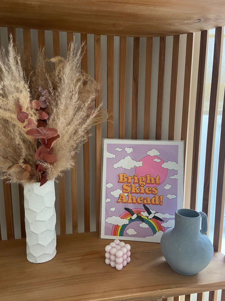 A vibrant printed poster titled 'Bright Skies Ahead' featuring uplifting imagery, designed by Ashley Molesso.