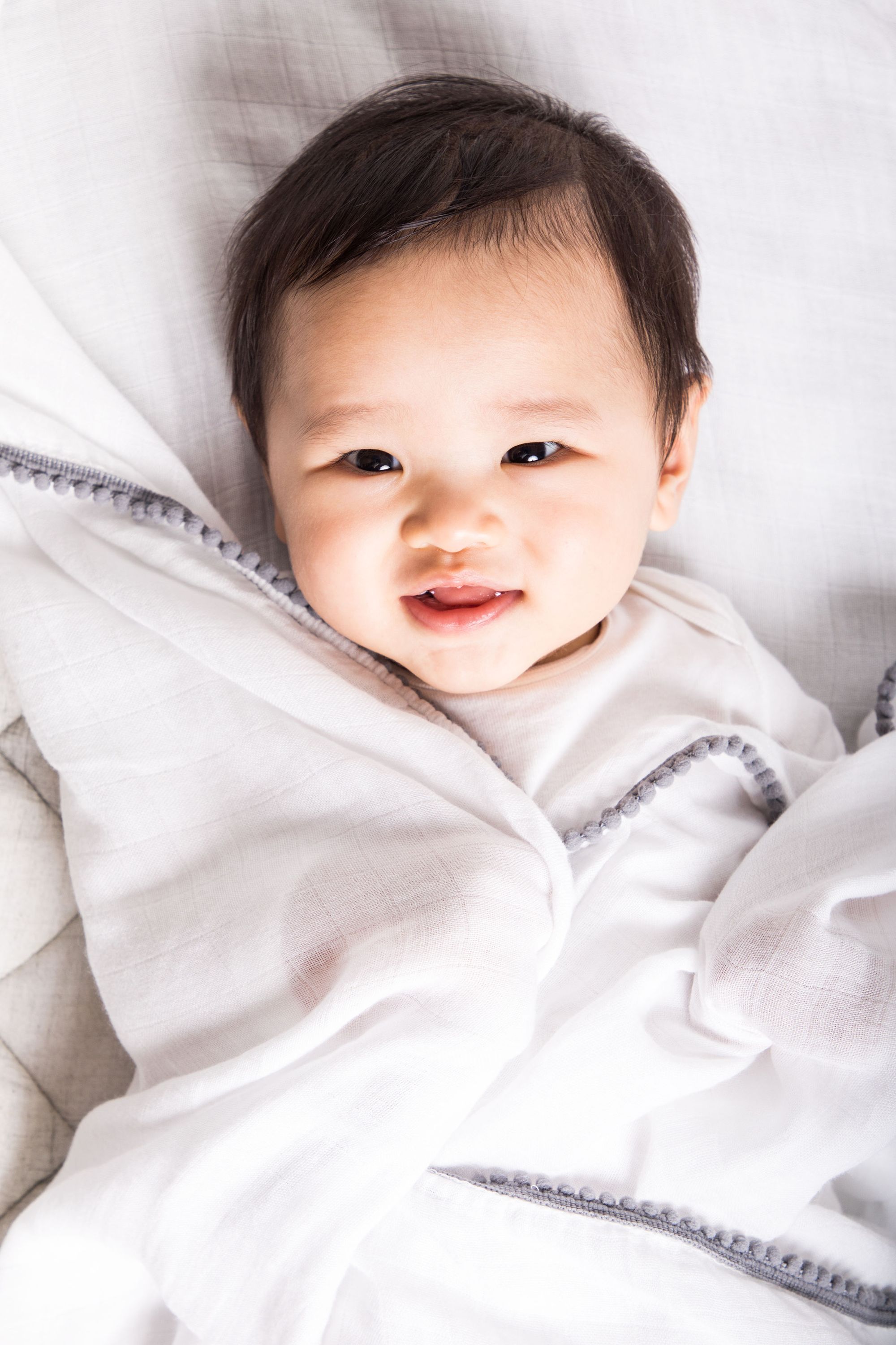 A soft bamboo and cotton swaddle featuring playful pom pom trim, perfect for newborns to toddlers.