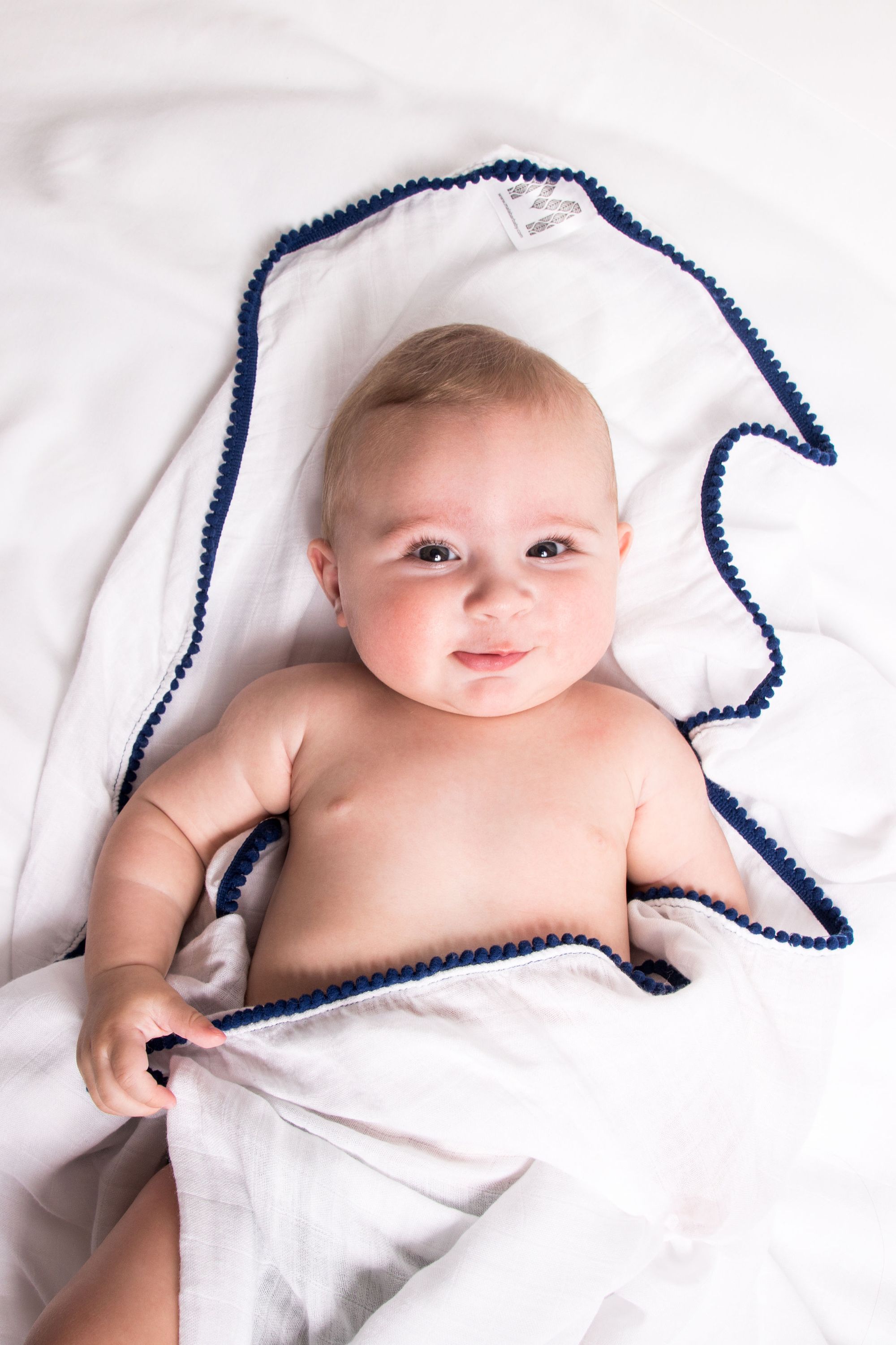 A soft bamboo and cotton swaddle featuring playful pom pom trim, perfect for newborns to toddlers.