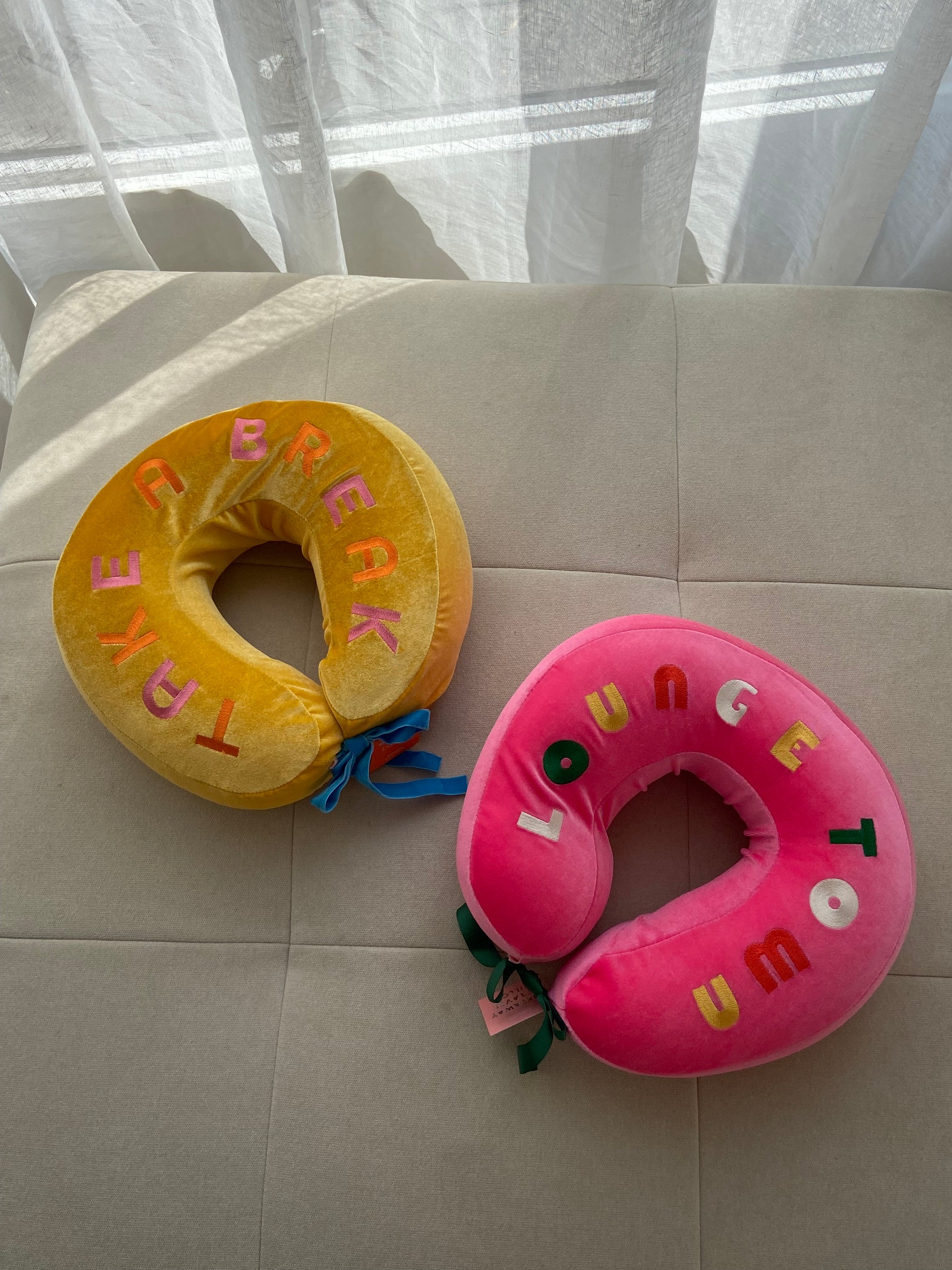 COUSSIN DE VOYAGE travel pillow in pink and yellow, featuring a soft removable cover and satin cord for easy attachment to luggage.