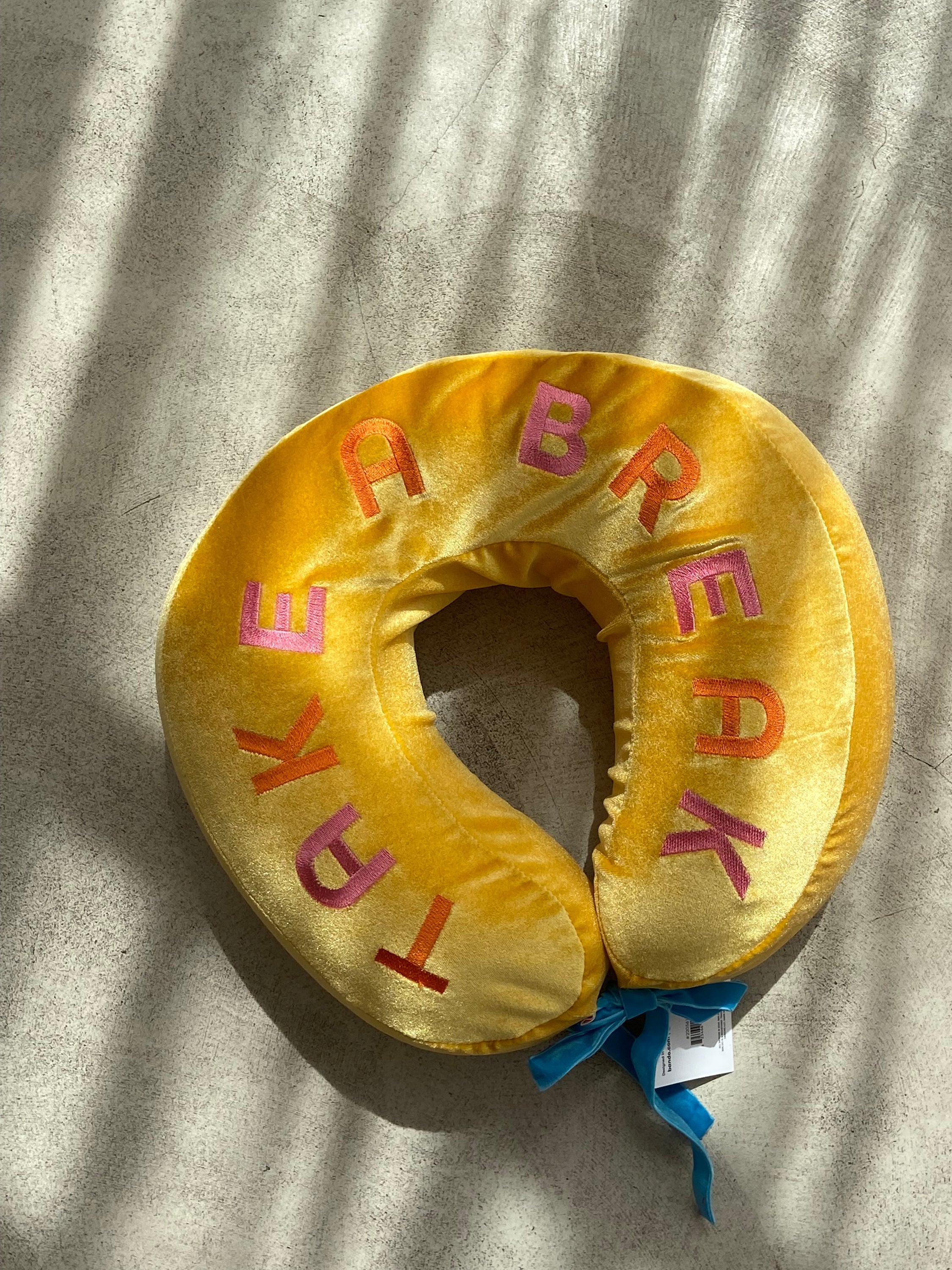 COUSSIN DE VOYAGE travel pillow in pink and yellow, featuring a soft removable cover and satin cord for easy attachment to luggage.