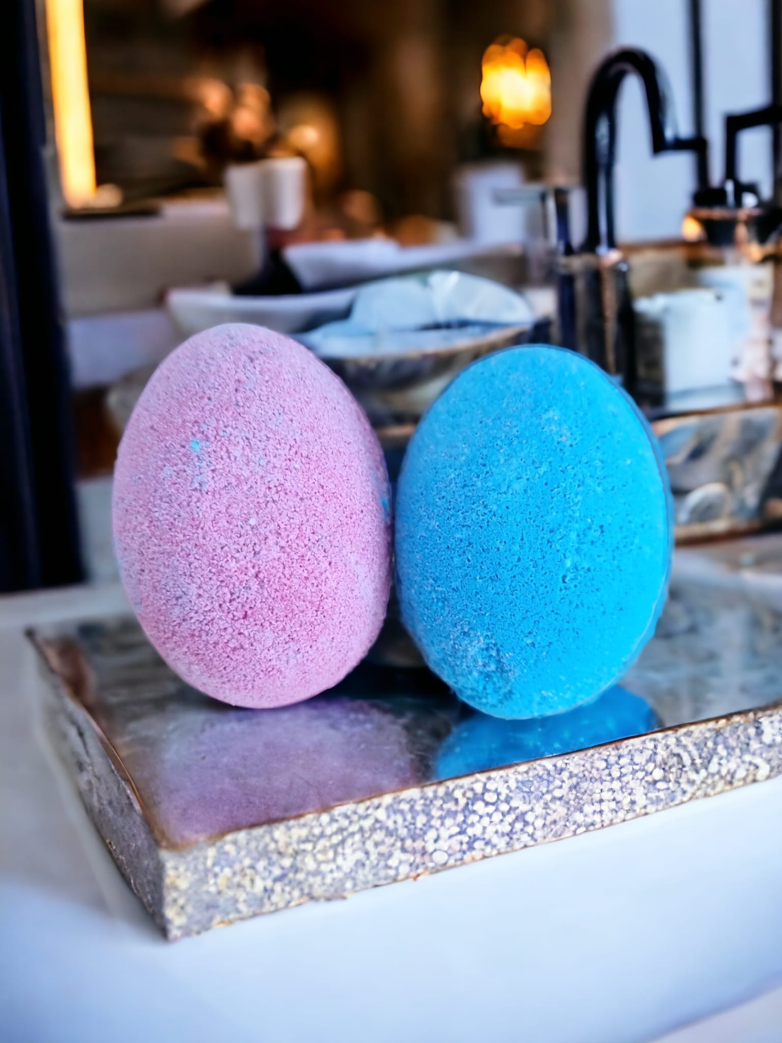 Two colorful egg-shaped bath bombs in purple and blue, packaged in a Kraft bag with an open window, showcasing their delightful design.