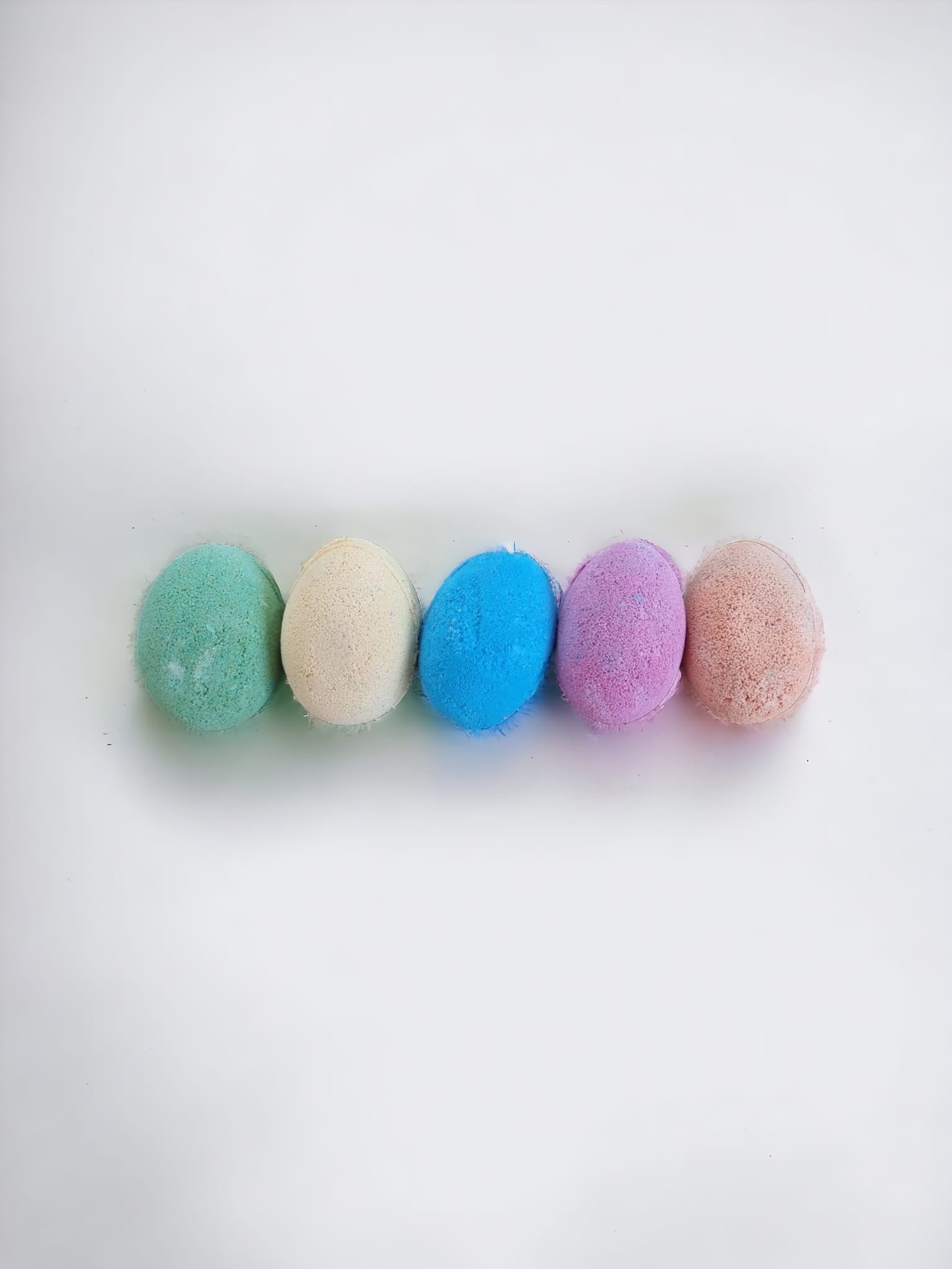 A colorful assortment of six Fizzy Egg Bath Bombs in purple, blue, yellow, green, and orange, beautifully arranged in a Kraft bag with an open window.