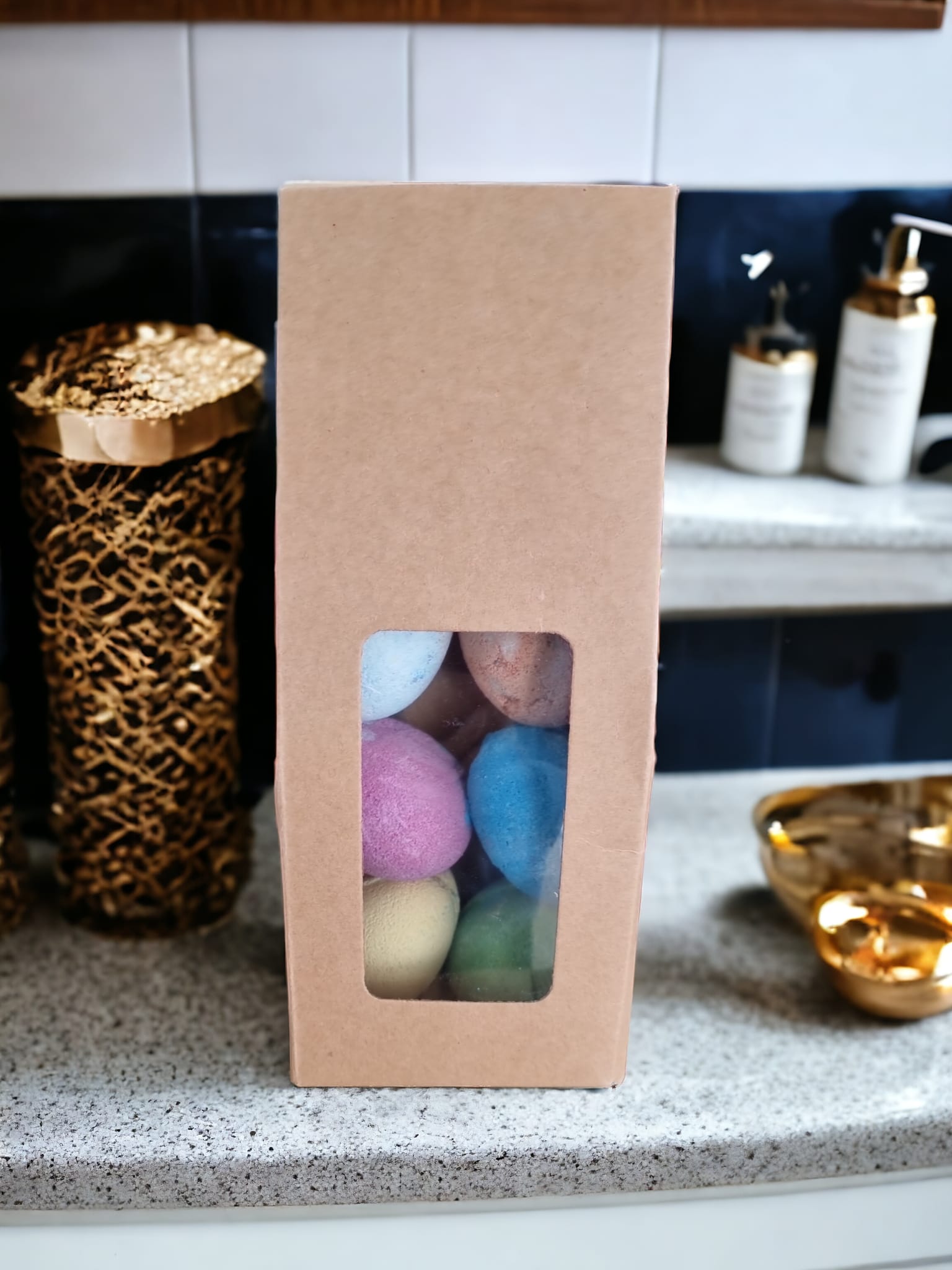 A colorful assortment of six Fizzy Egg Bath Bombs in purple, blue, yellow, green, and orange, beautifully arranged in a Kraft bag with an open window.
