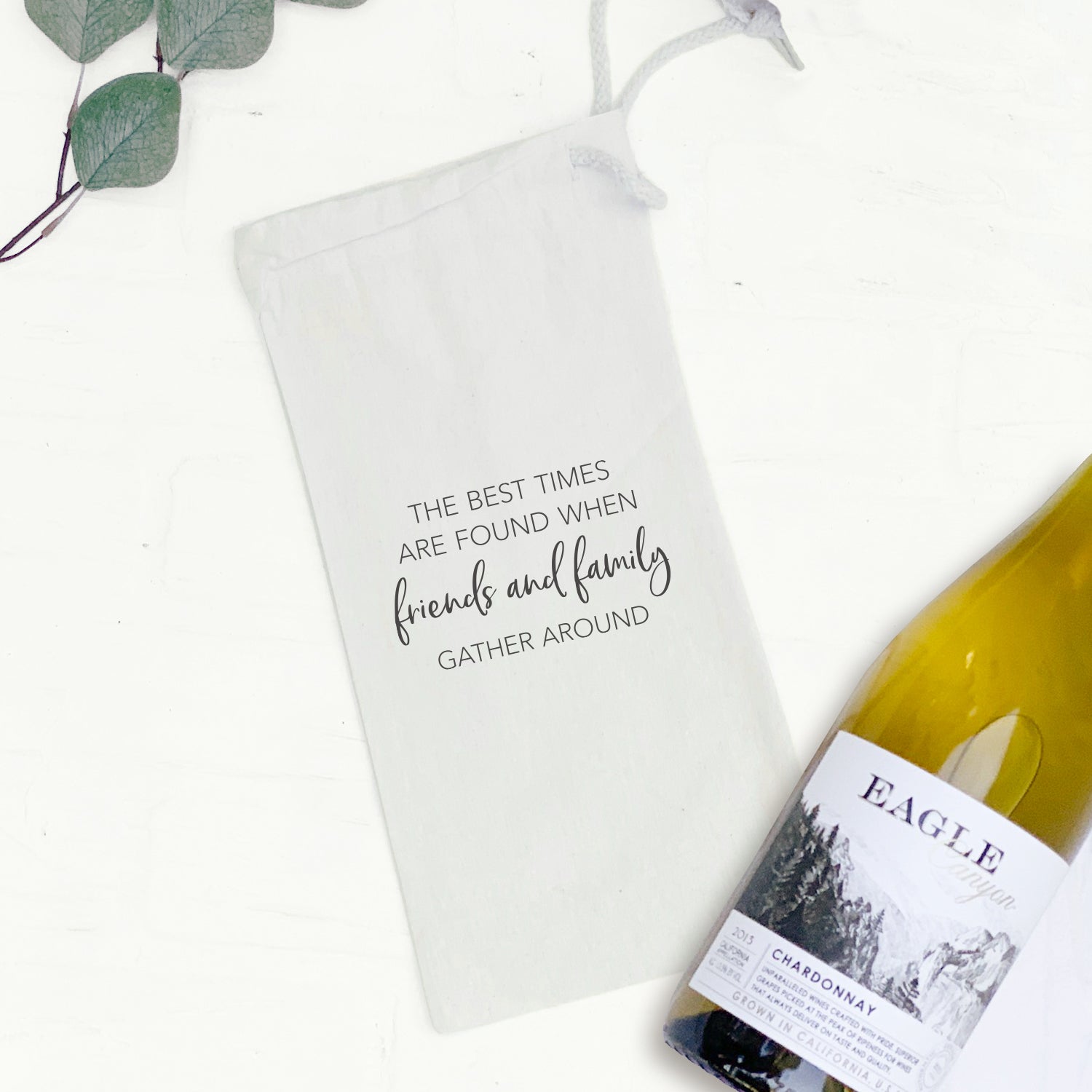 A stylish Friends Family Gather Around canvas wine bag featuring a matching drawstring closure, designed to hold a standard 750mL wine bottle.