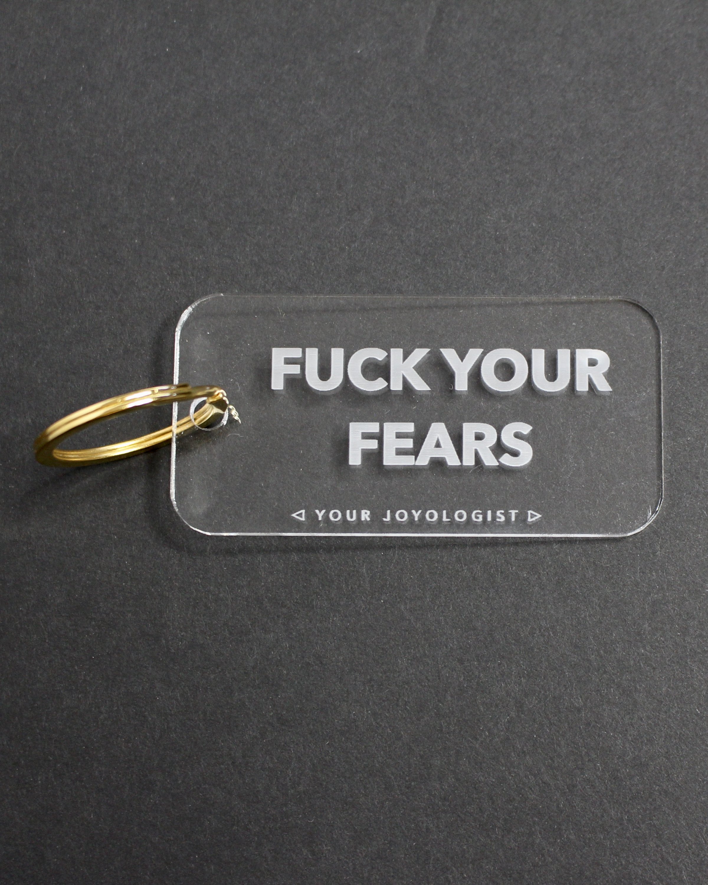 Clear acrylic key chain with 'Fuck Your Fears' engraved, attached to a gold key ring.