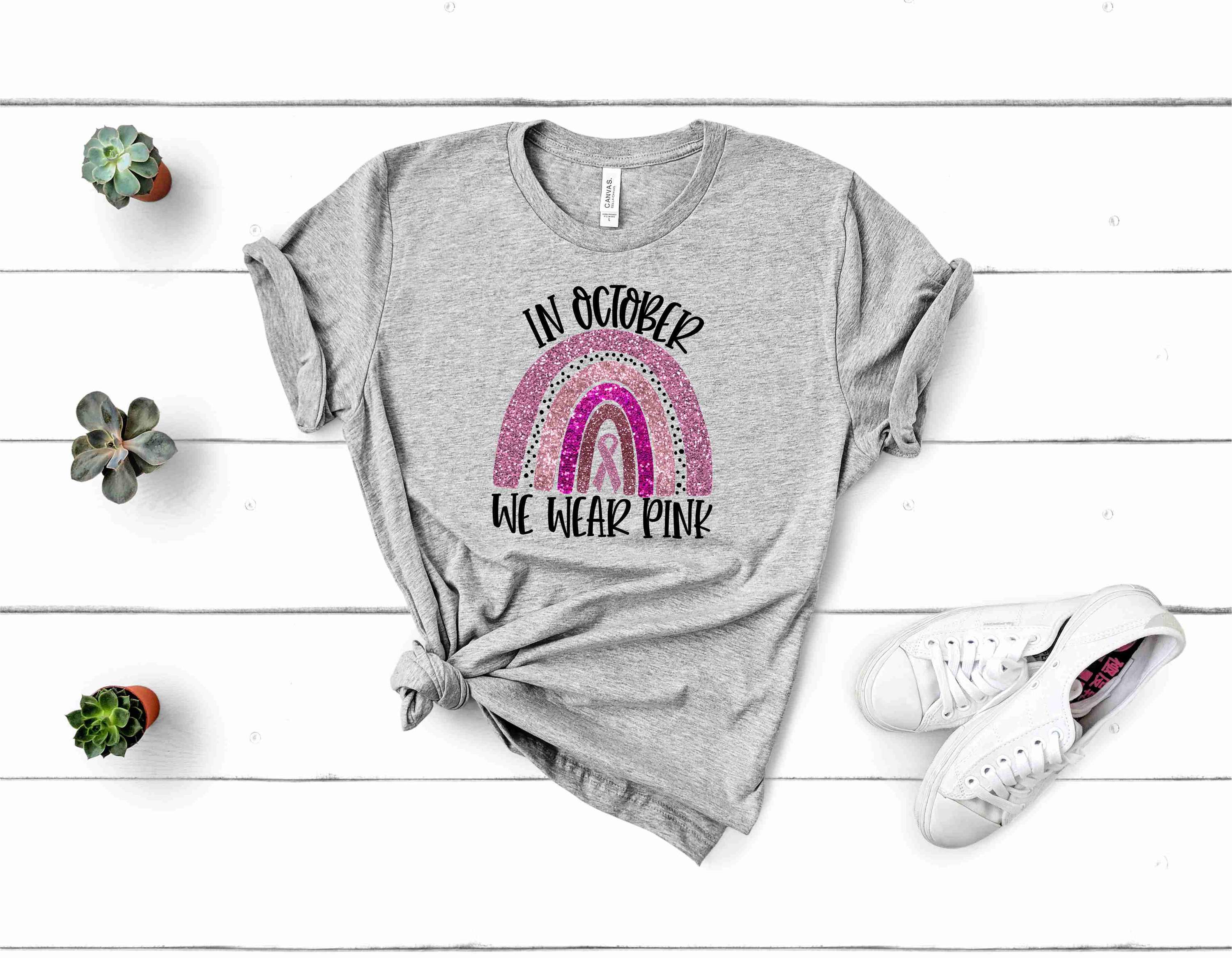 Grey graphic tee featuring 'In October We Wear Pink' design, made from soft Bella Canvas fabric, suitable for unisex wear.