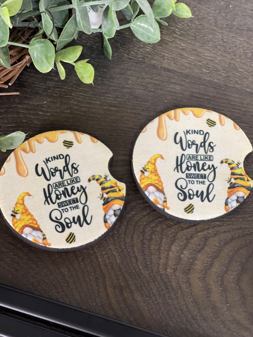 A set of two neoprene car coasters featuring the phrase 'Kind Words Are Like Honey' in a vibrant design, perfect for cup holders.