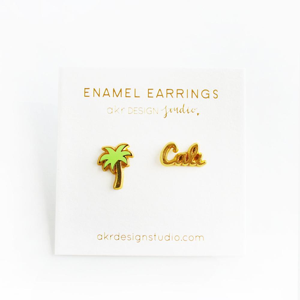 A pair of stylish Palm Tree & Cali Earrings made of hard enamel, featuring a palm tree design and a butterfly stopper.