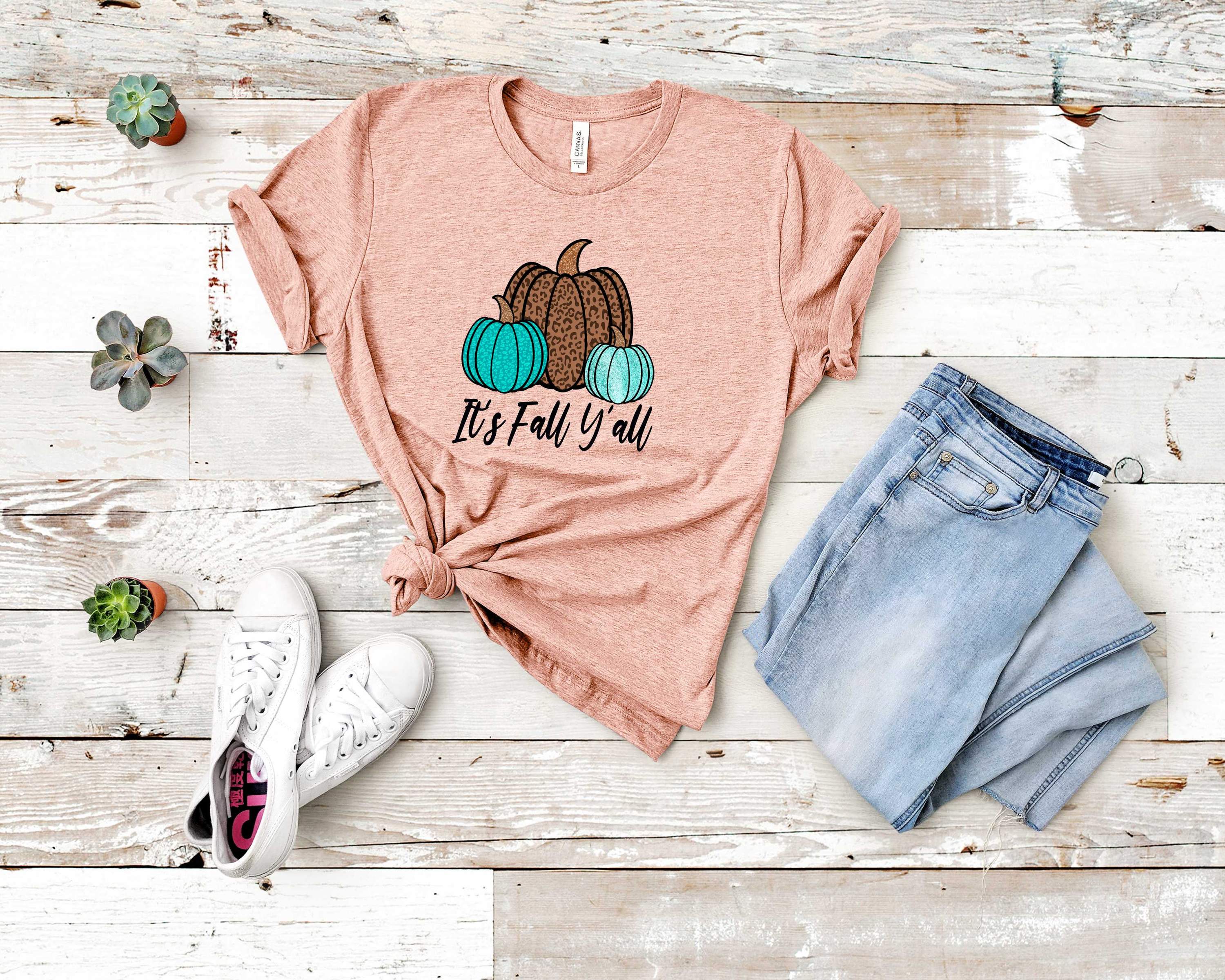 Teal graphic tee with 'It's Fall Y'all' text, made from soft Bella Canvas fabric, perfect for autumn wear.
