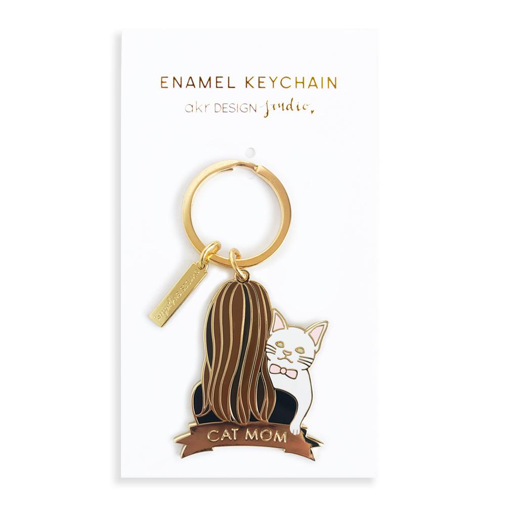 A charming white cat keychain featuring brunette hair, crafted from high-quality hard enamel, presented on a stylish backing card.