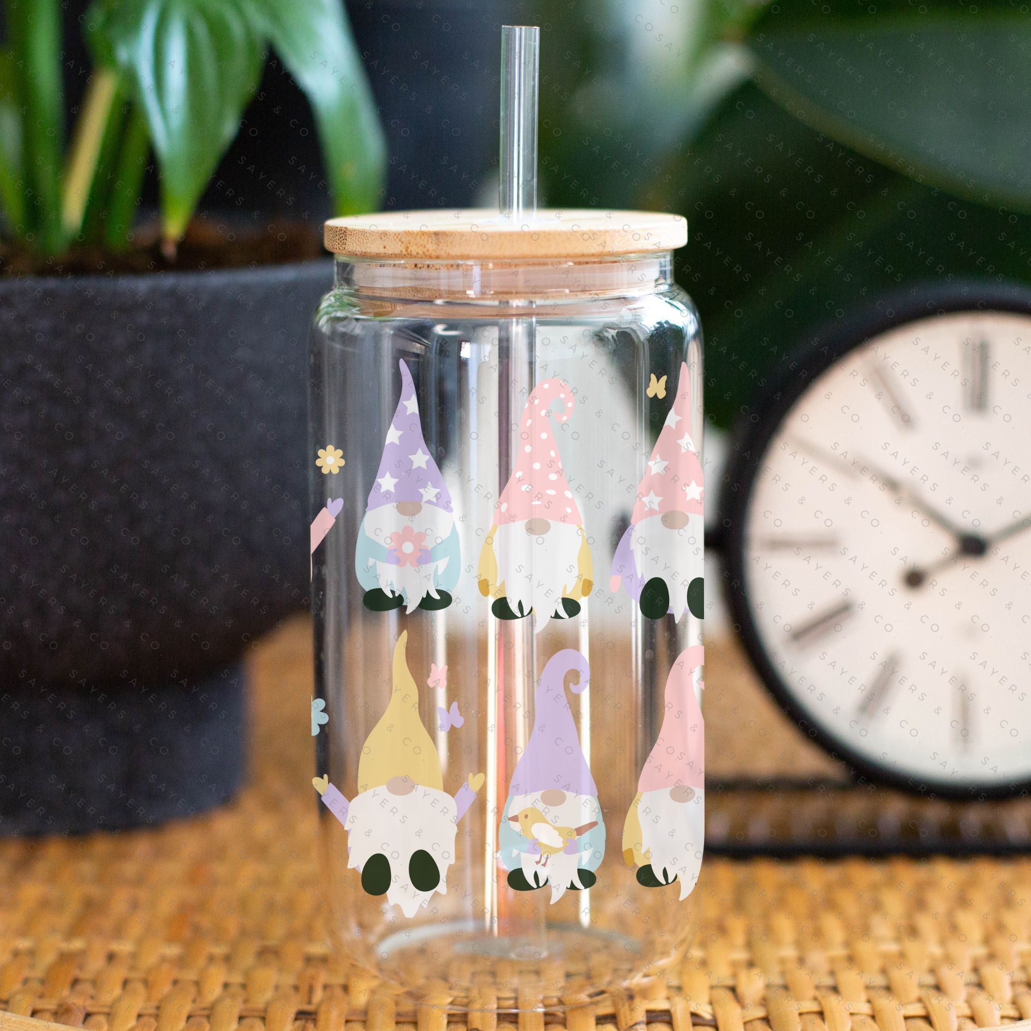 A 16oz clear glass cup featuring a whimsical spring gnome design, complete with a bamboo lid and a clear plastic straw, perfect for various beverages.