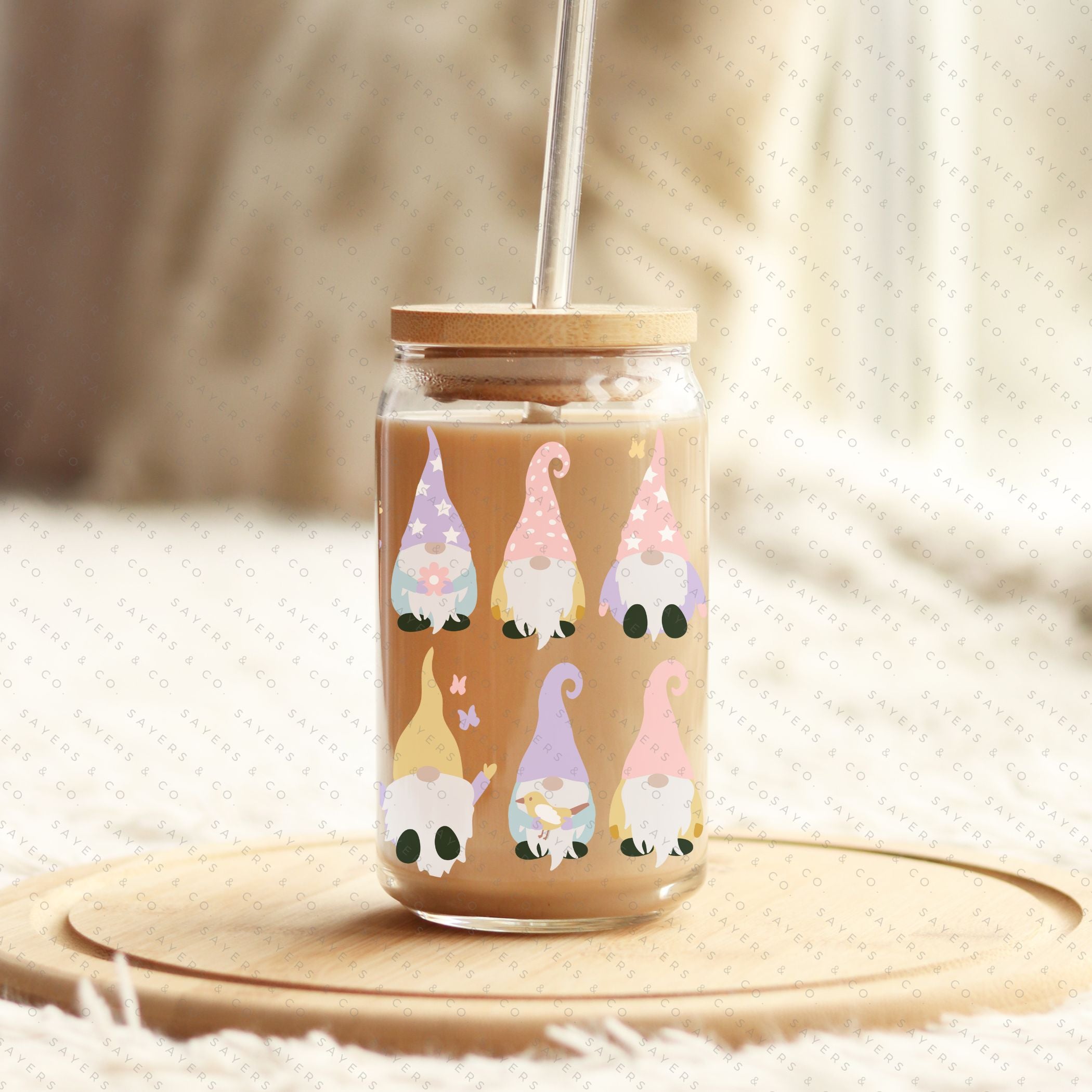 A 16oz clear glass cup featuring a whimsical spring gnome design, complete with a bamboo lid and a clear plastic straw, perfect for various beverages.