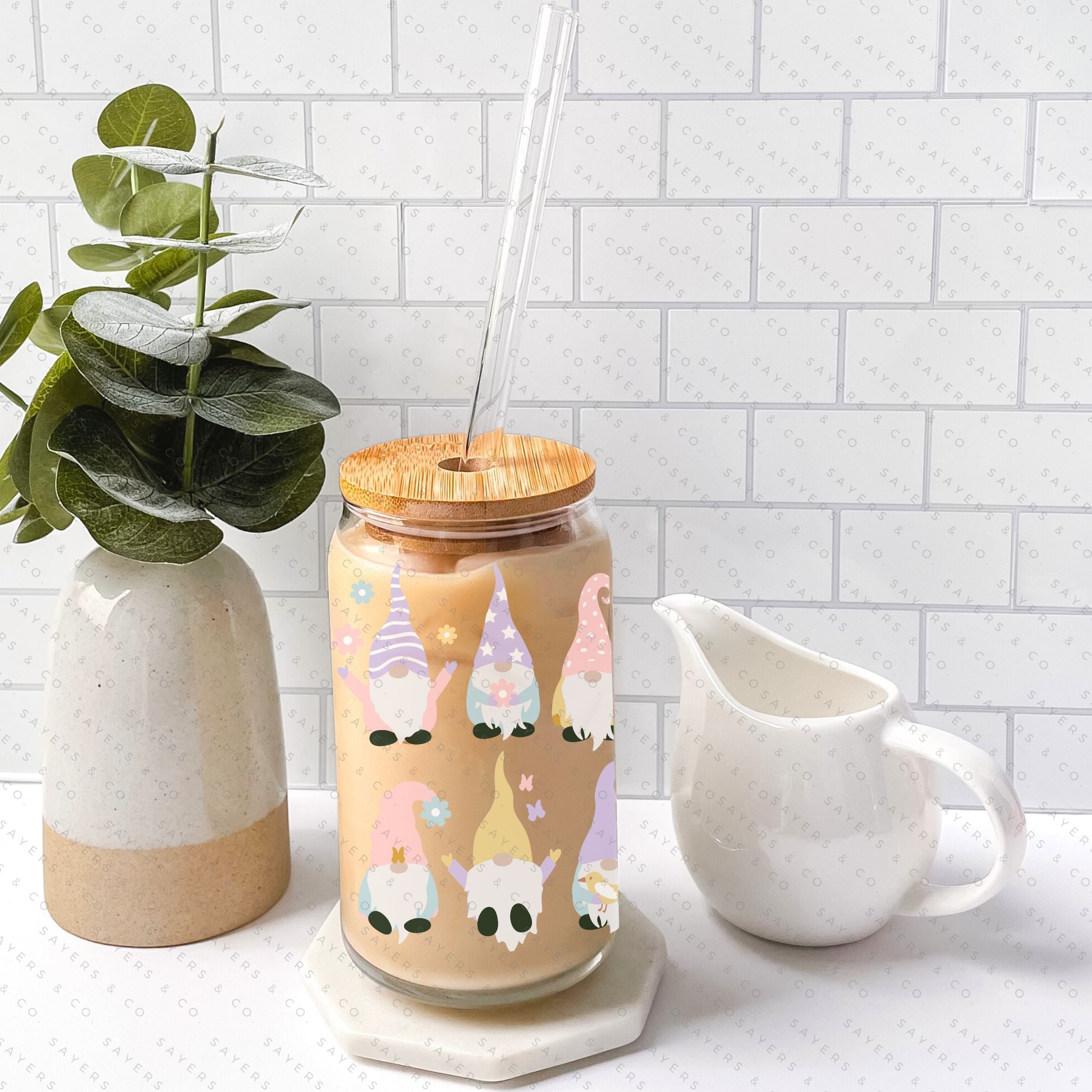 A 16oz clear glass cup featuring a whimsical spring gnome design, complete with a bamboo lid and a clear plastic straw, perfect for various beverages.