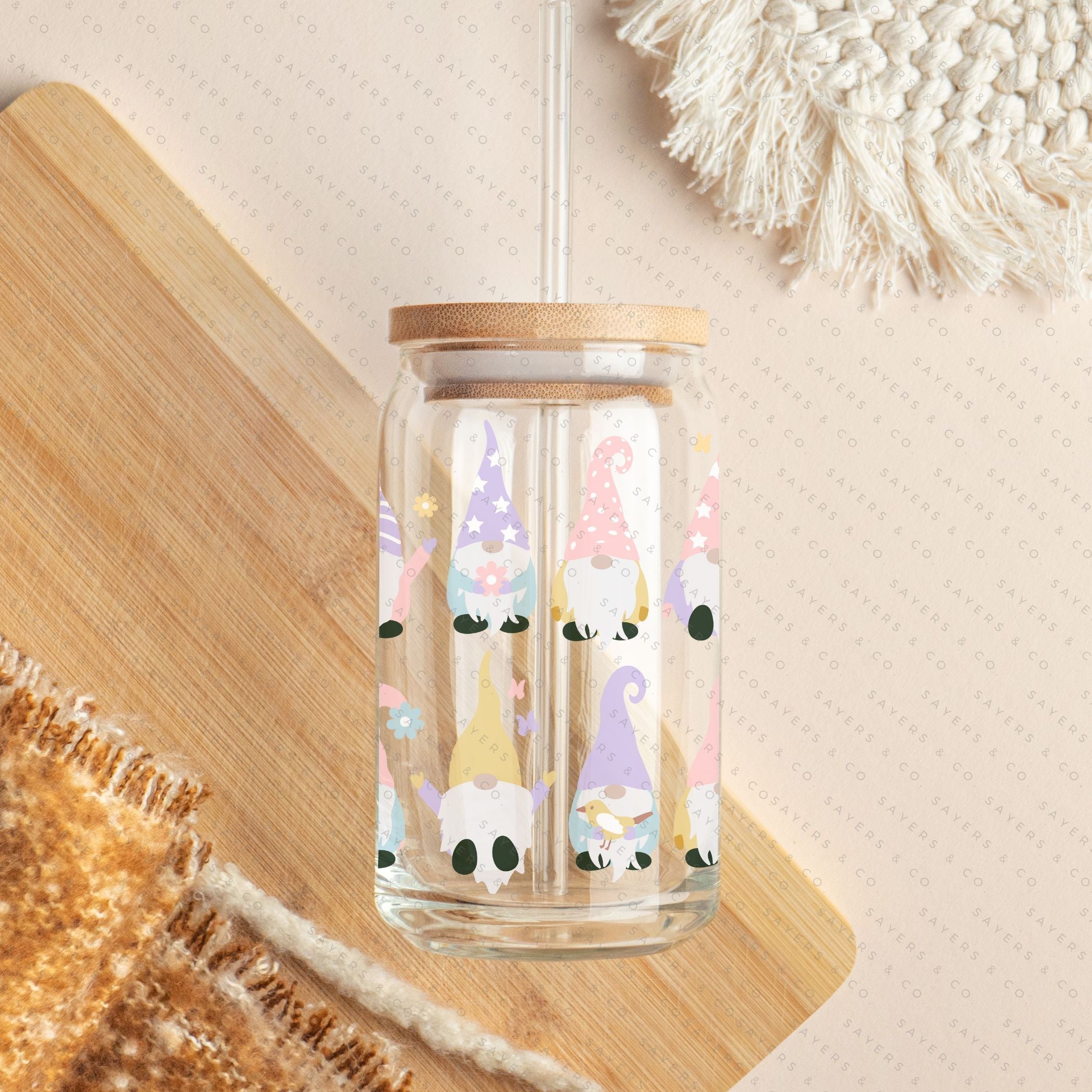 A 16oz clear glass cup featuring a whimsical spring gnome design, complete with a bamboo lid and a clear plastic straw, perfect for various beverages.