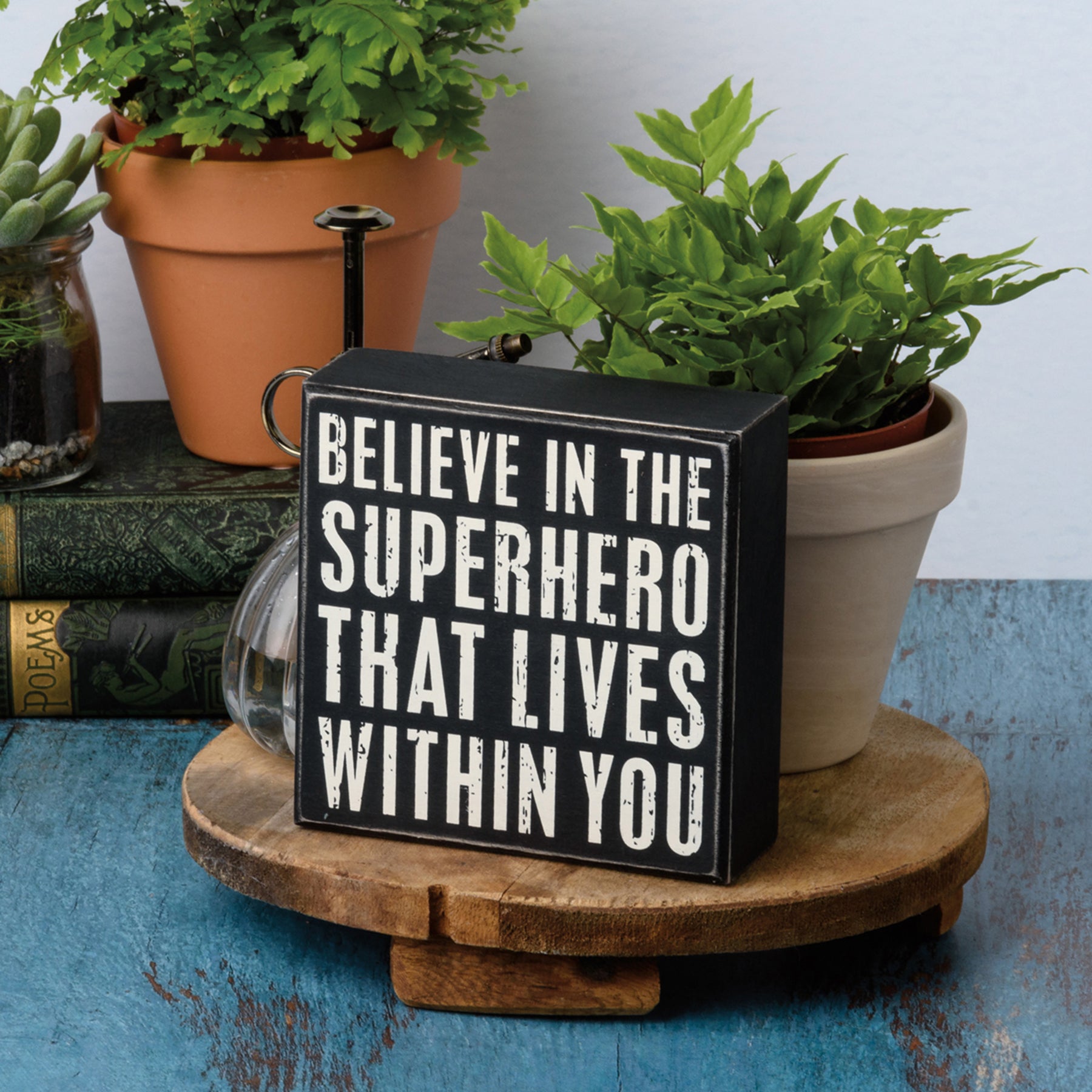 A black and white wooden box sign with the phrase 'Believe In The Superhero That Lives Within You' in a distressed finish, perfect for home decor.