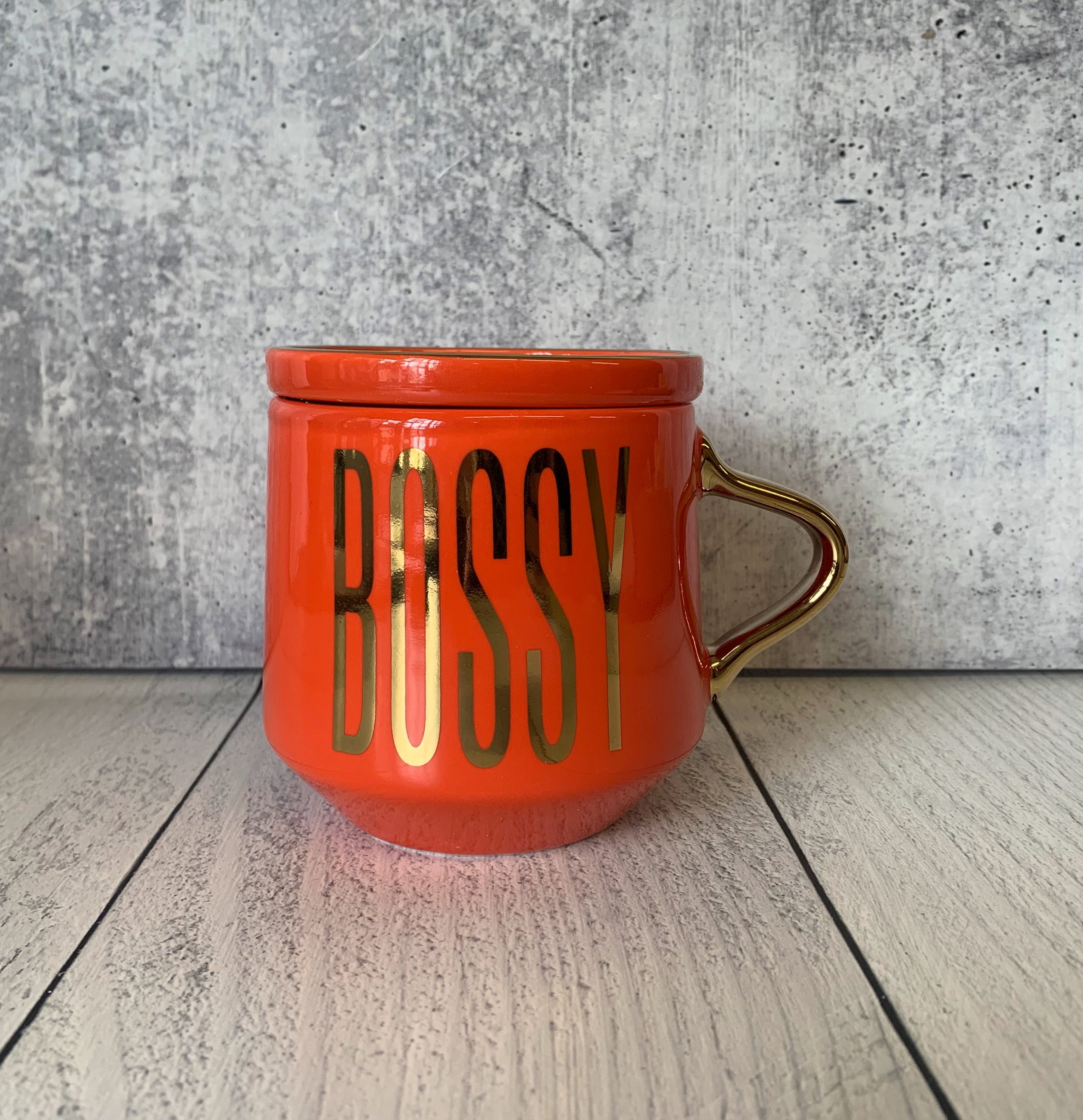 A stylish red and gold ceramic mug with 'BOSSY' printed on it, accompanied by a matching coaster lid.