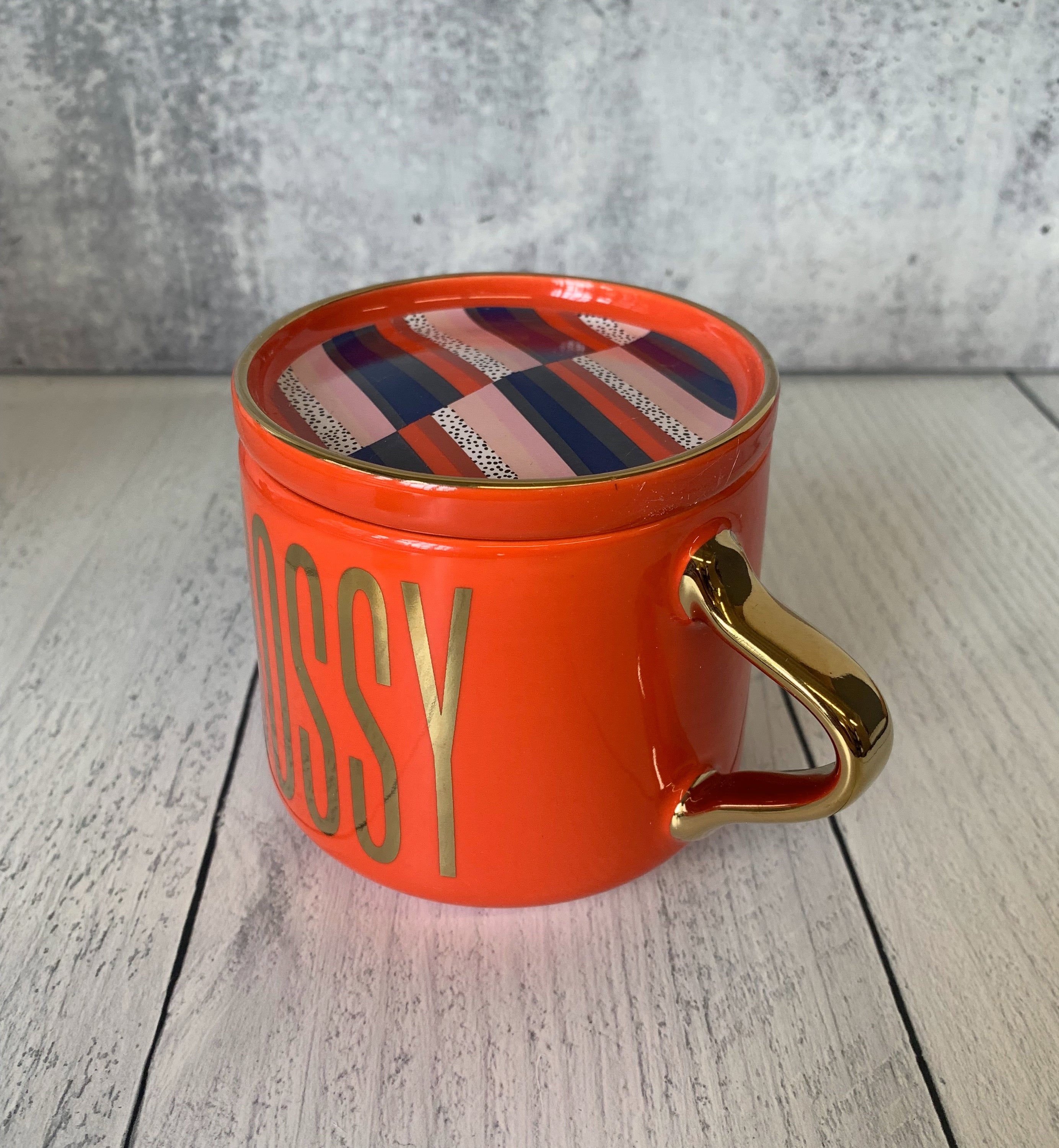 A stylish red and gold ceramic mug with 'BOSSY' printed on it, accompanied by a matching coaster lid.