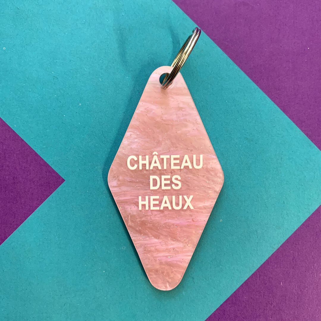Chateau Des Heaux Motel Style Keychain in Crystal Pink with white lettering, featuring a split ring for key attachment.
