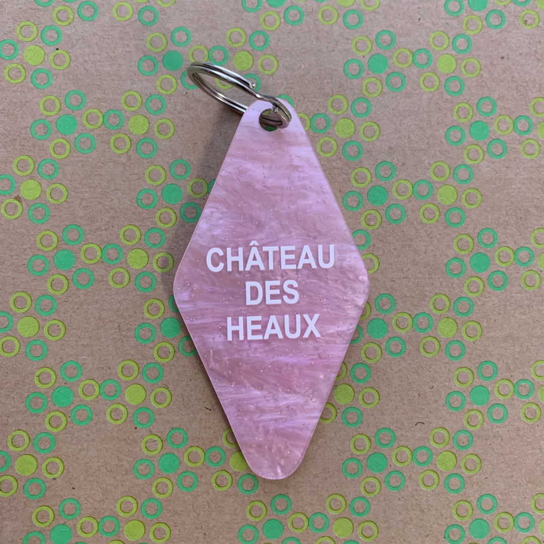 Chateau Des Heaux Motel Style Keychain in Crystal Pink with white lettering, featuring a split ring for key attachment.
