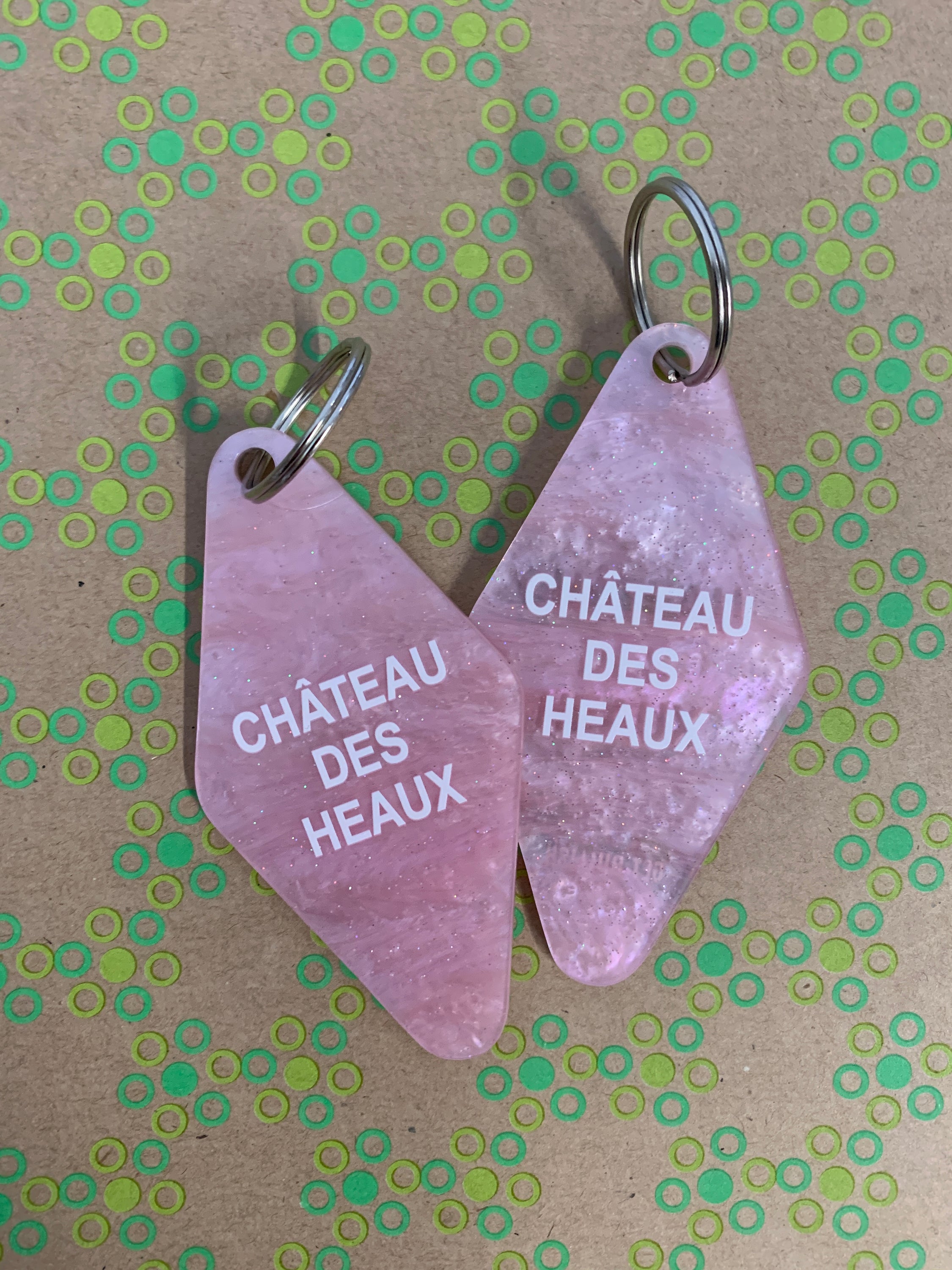 Chateau Des Heaux Motel Style Keychain in Crystal Pink with white lettering, featuring a split ring for key attachment.