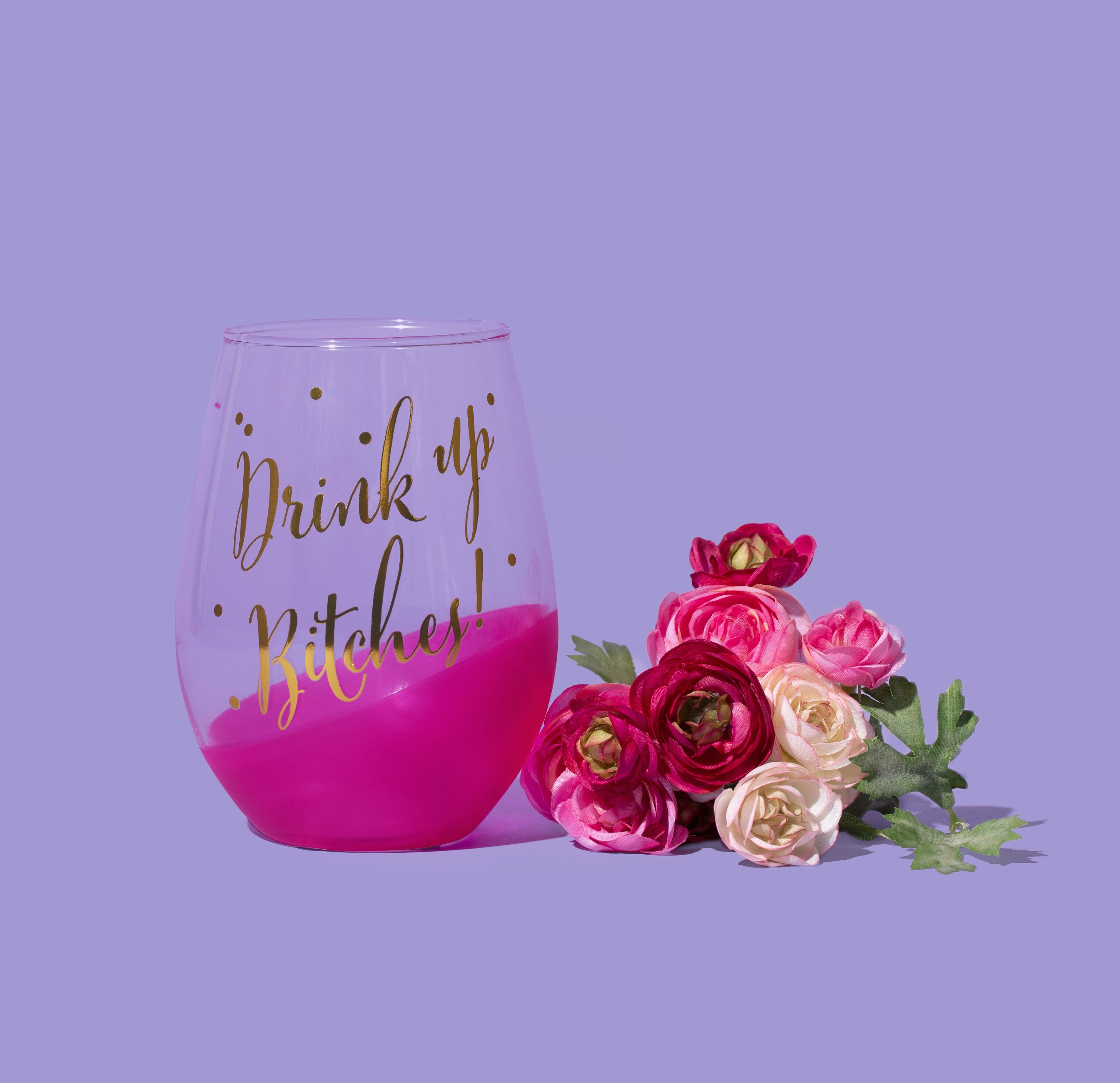 A stylish stemless wine glass with gold lettering that reads 'Drink Up Bitches!', featuring a pink slant detail and gold polka dots.