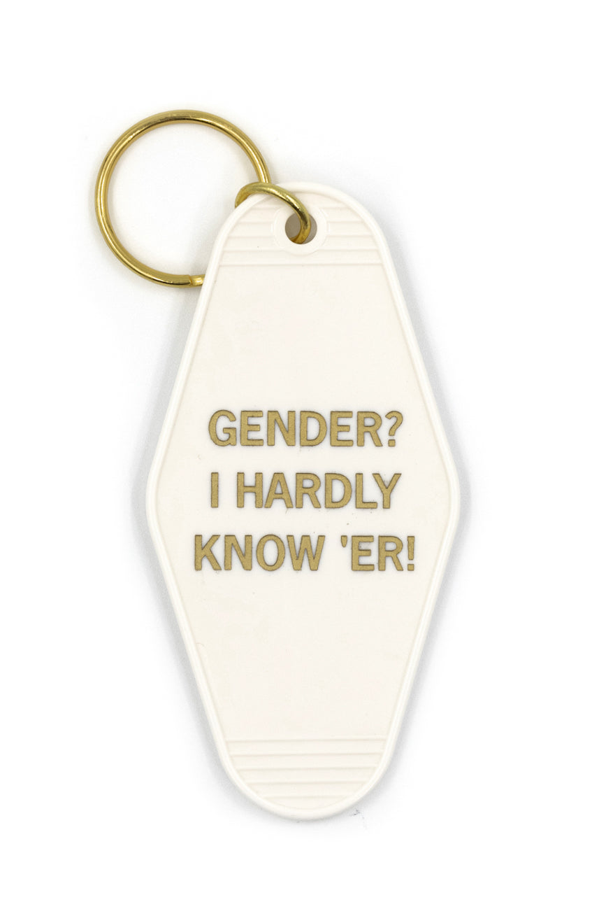 White and gold motel-style keychain with the phrase 'GENDER? I HARDLY KNOW 'ER' in gold lettering, attached to a split ring.