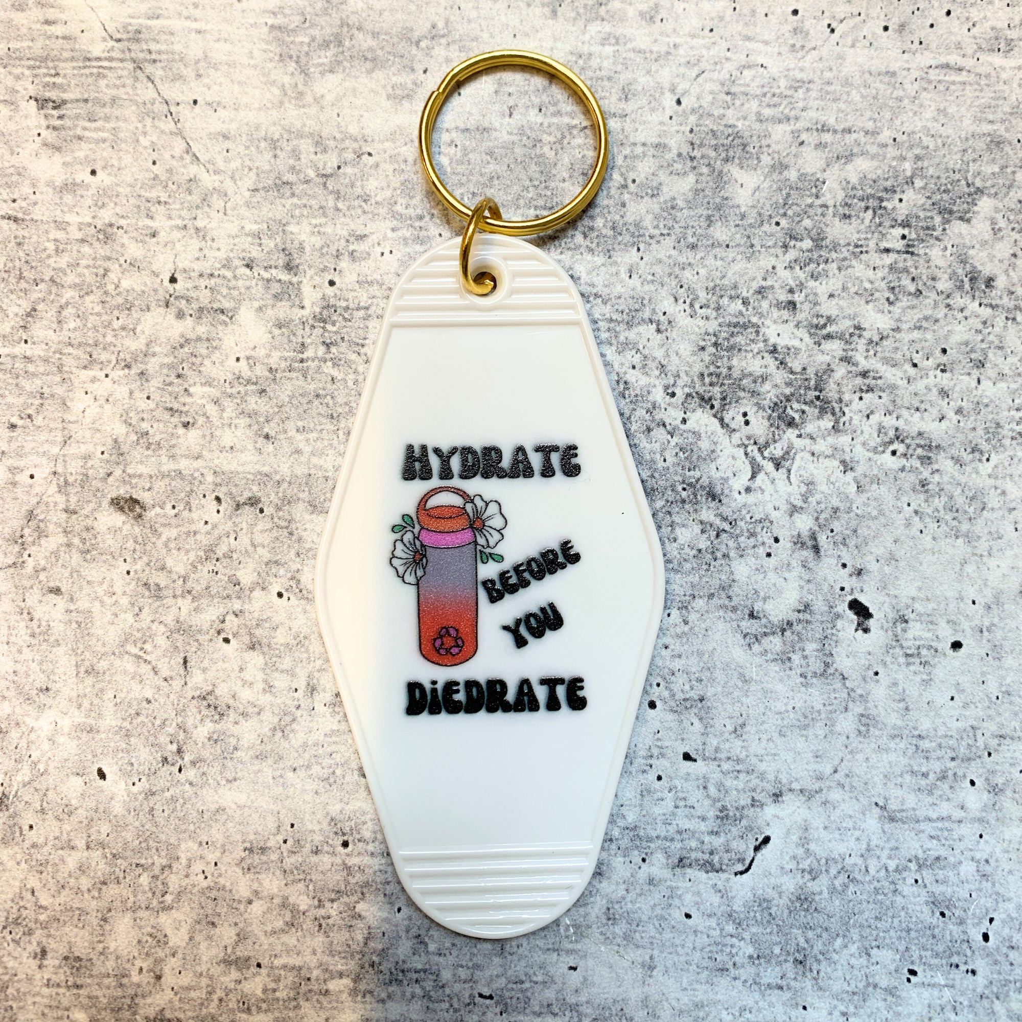 A vibrant motel style keychain with the phrase 'Hydrate Before You Diedrate' in bold letters, featuring a split ring for easy attachment.