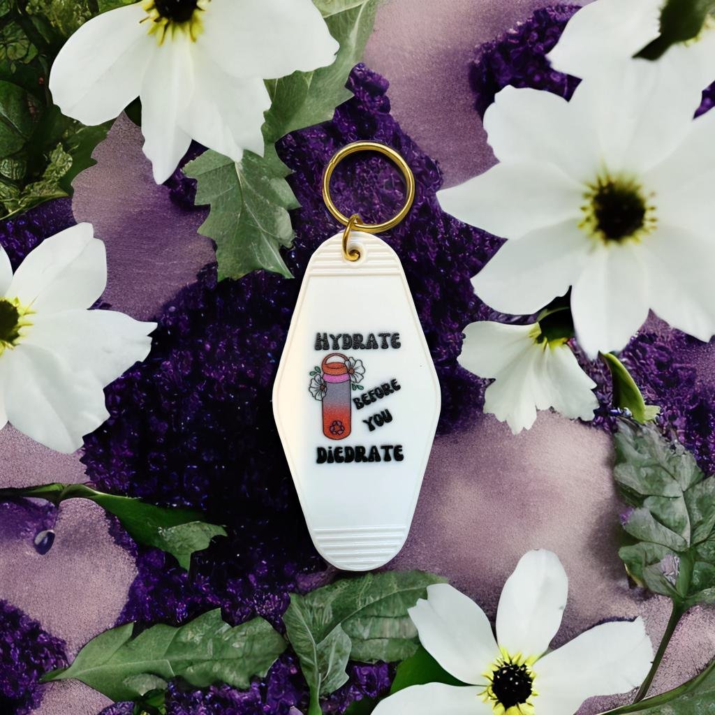 A vibrant motel style keychain with the phrase 'Hydrate Before You Diedrate' in bold letters, featuring a split ring for easy attachment.