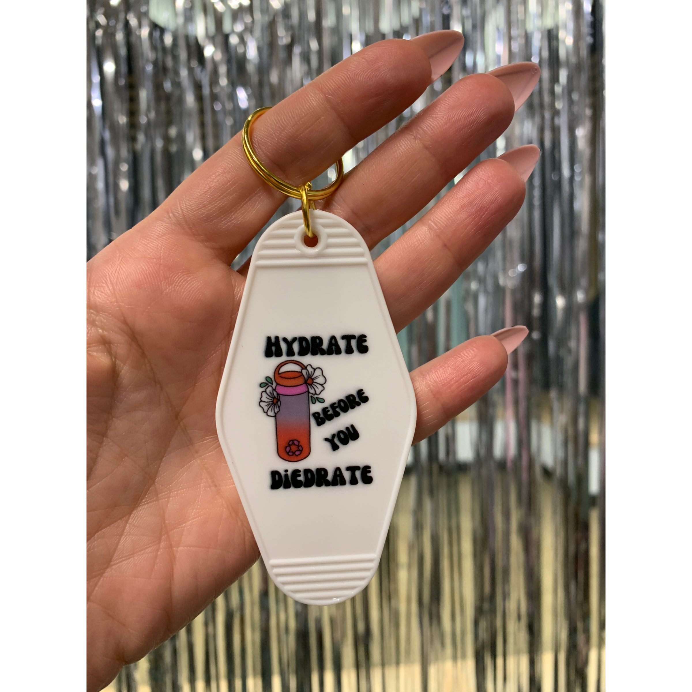 A vibrant motel style keychain with the phrase 'Hydrate Before You Diedrate' in bold letters, featuring a split ring for easy attachment.