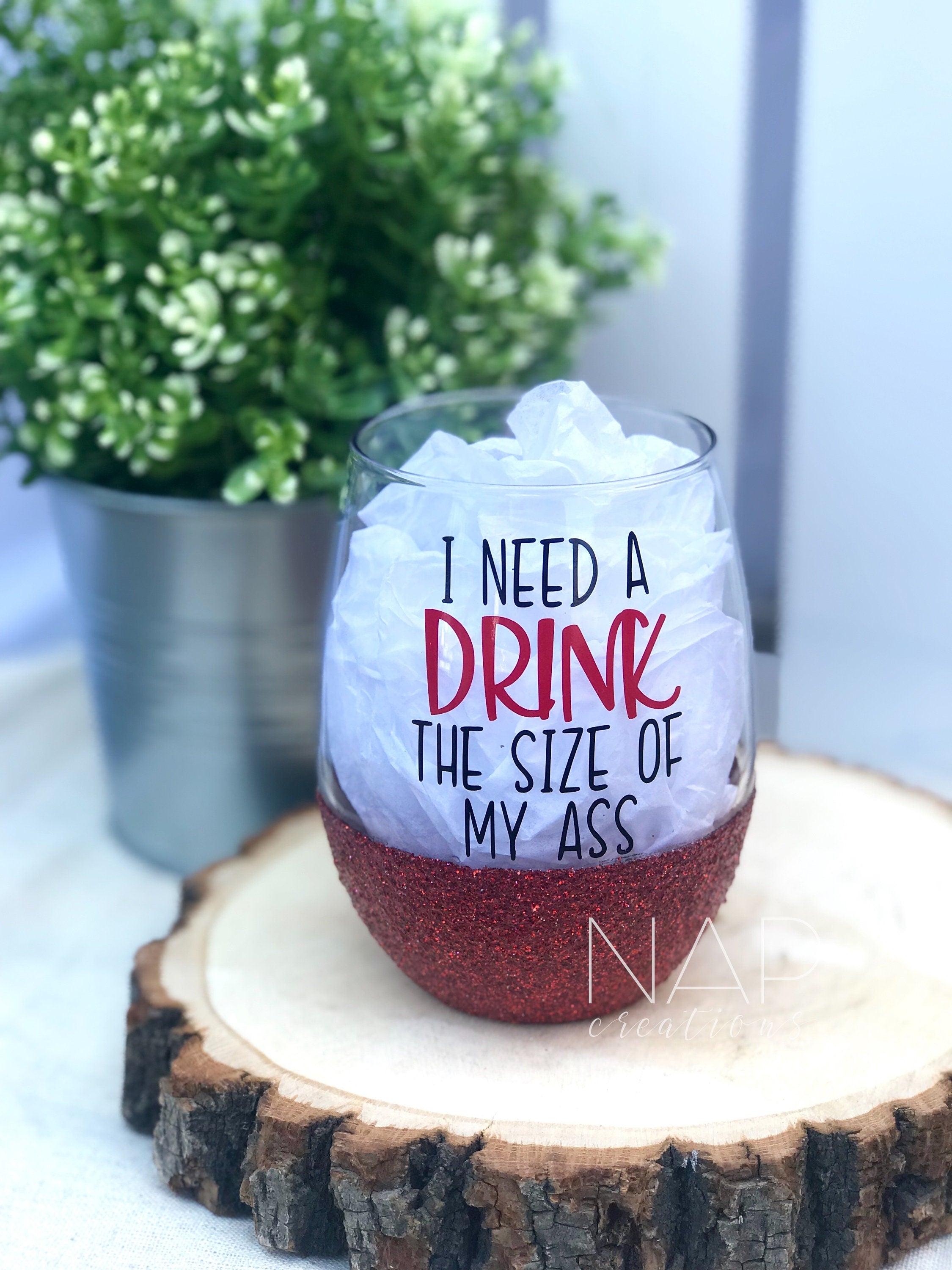 A stylish stemless wine glass with glitter and the phrase 'I Need A Drink The Size Of My Ass' printed on one side, showcasing vibrant colors.
