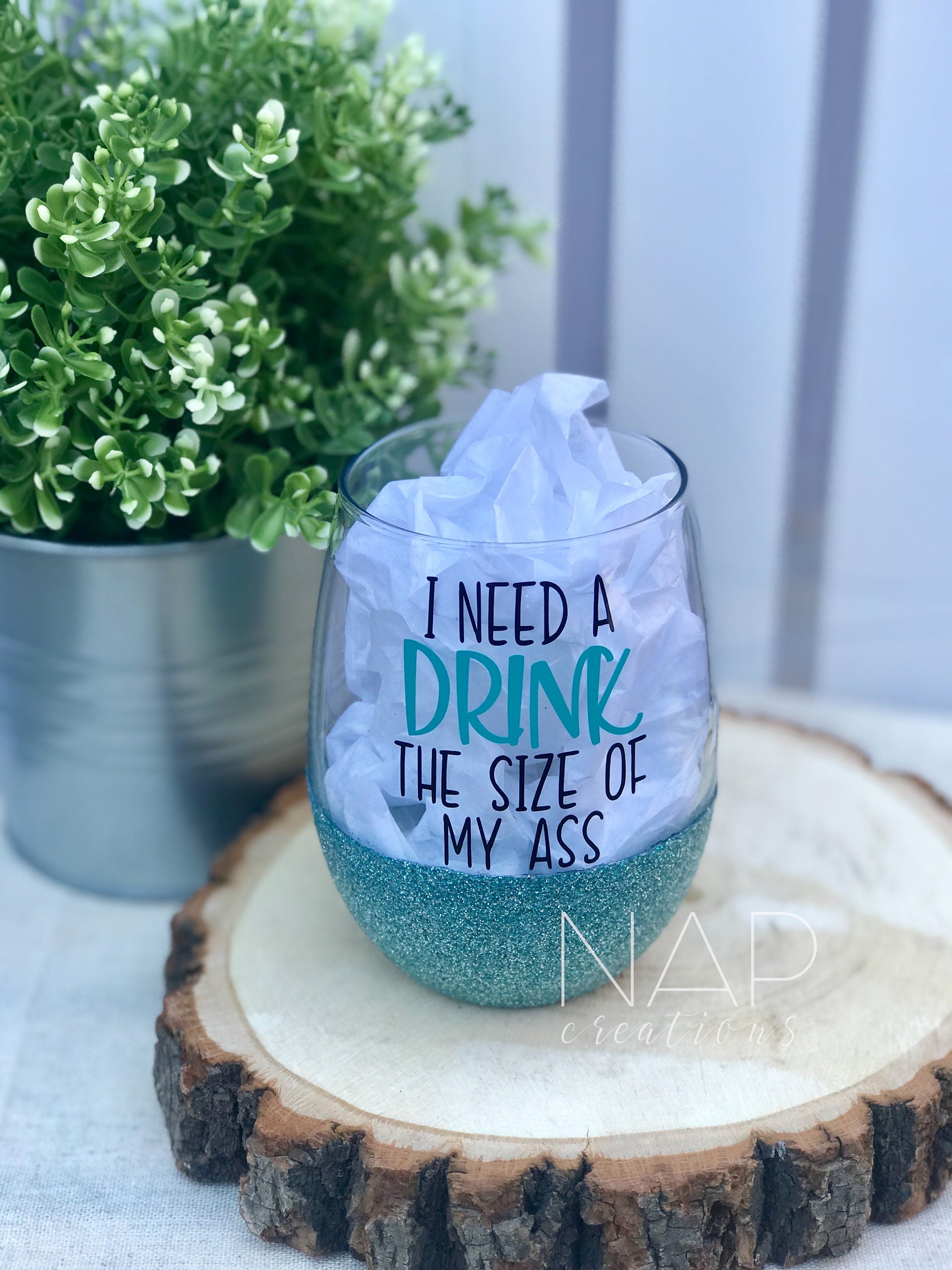 A stylish stemless wine glass with glitter and the phrase 'I Need A Drink The Size Of My Ass' printed on one side, showcasing vibrant colors.