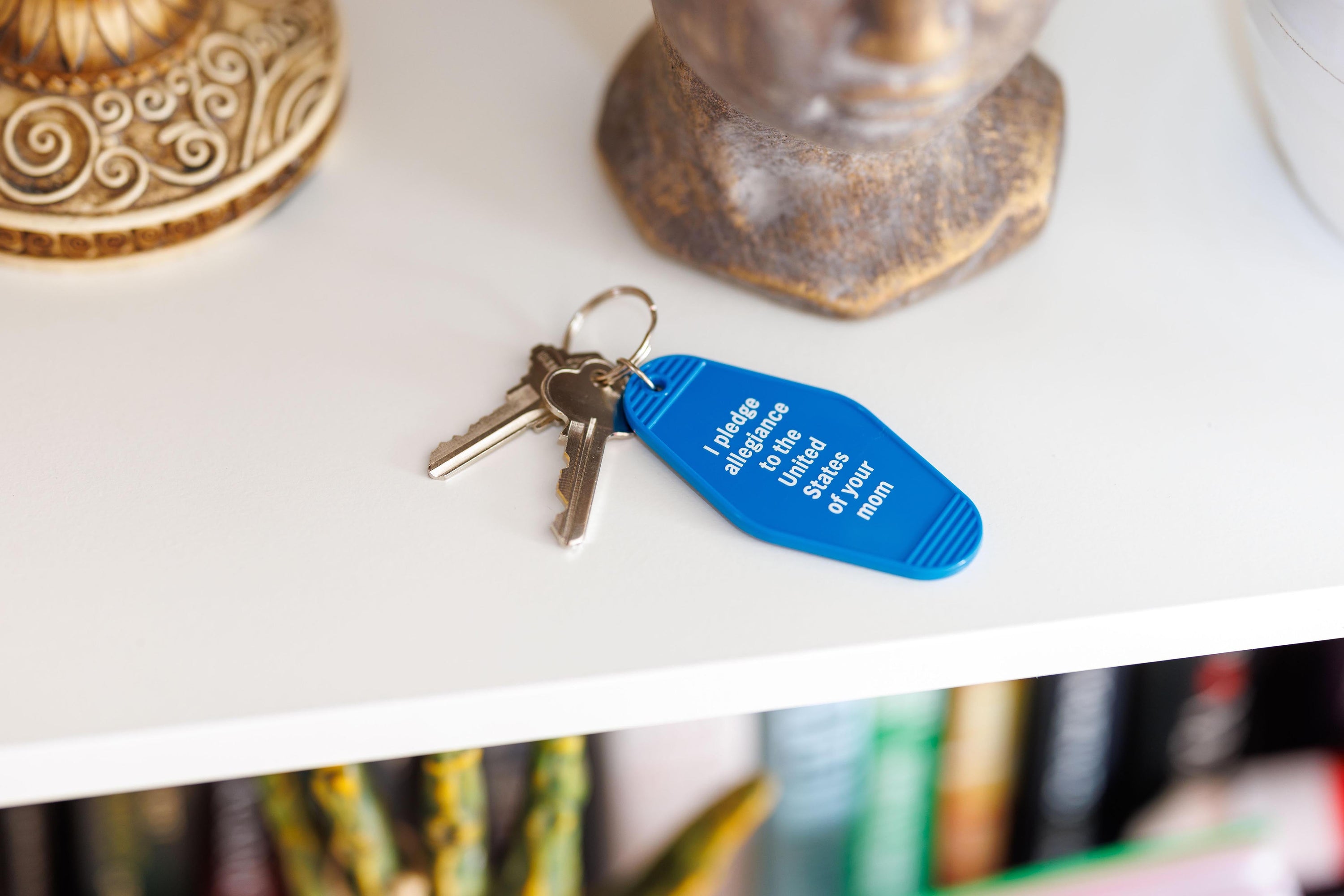 Blue motel keychain with the phrase 'I Pledge Allegiance to the United States of Your Mom' and a split ring attachment.