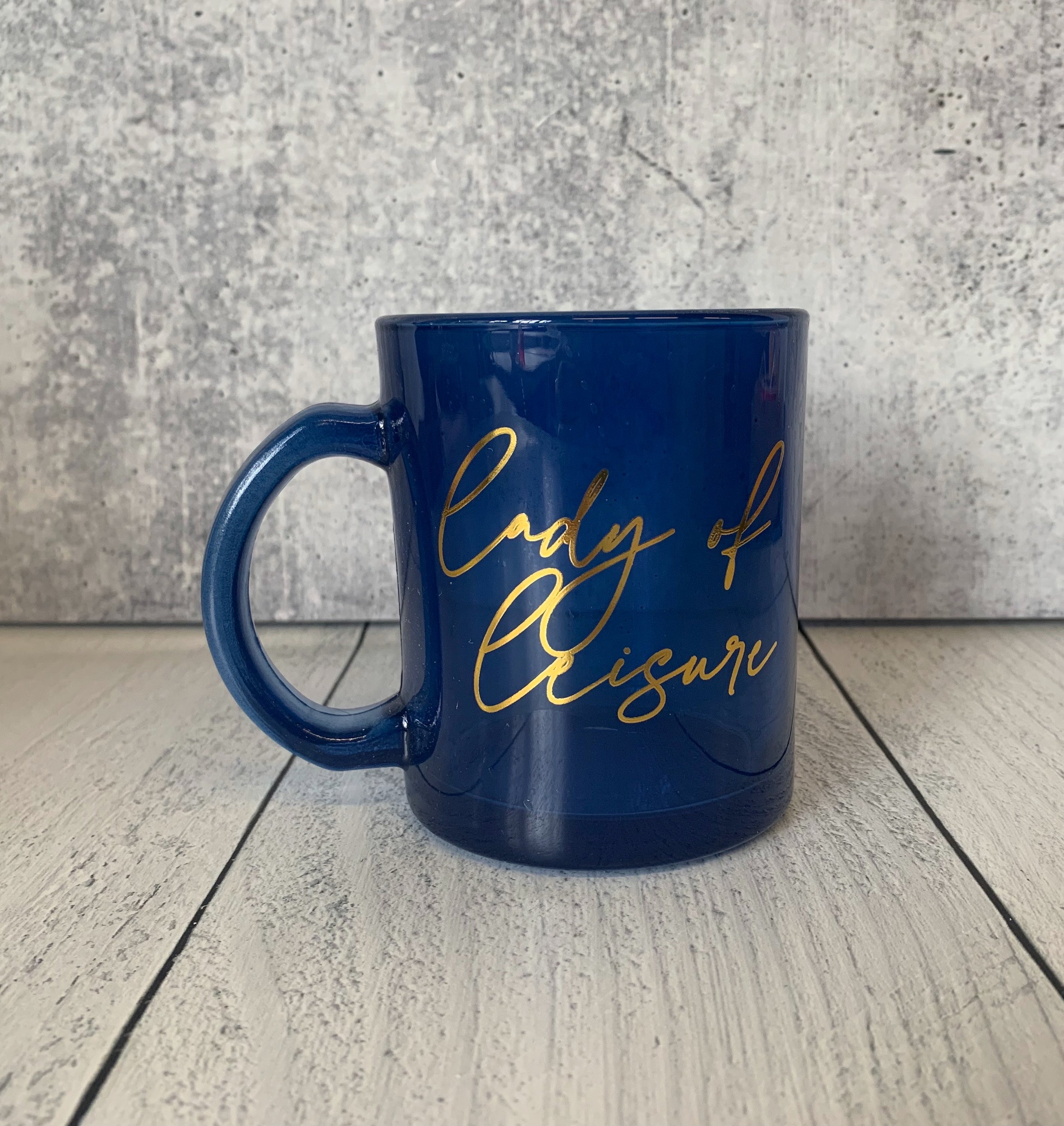 Lady of Leisure Single-Wall Glass Mug in dark blue tinted glass with gold lettering, elegantly designed for stylish sipping.