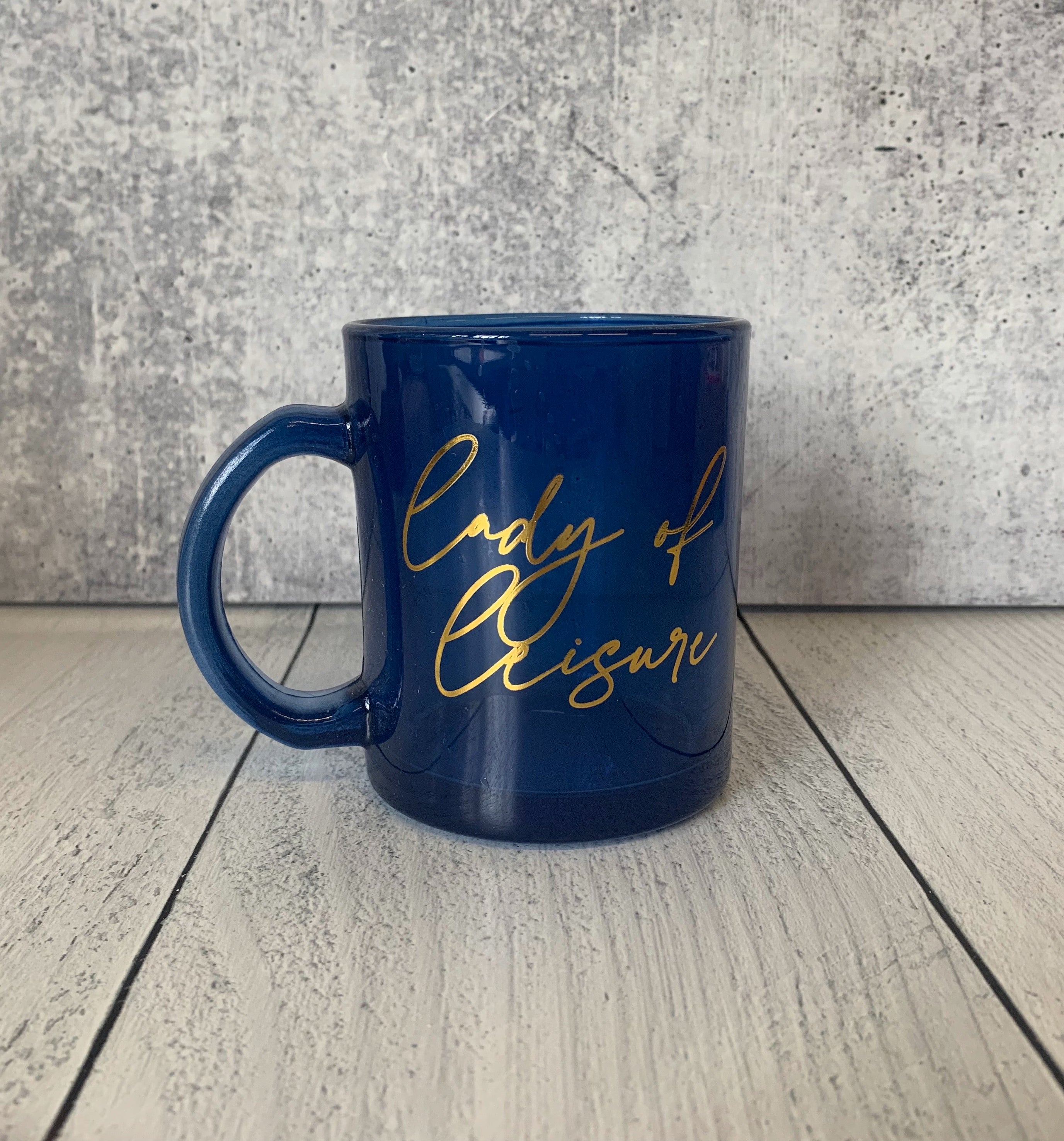 Lady of Leisure Single-Wall Glass Mug in dark blue tinted glass with gold lettering, elegantly designed for stylish sipping.