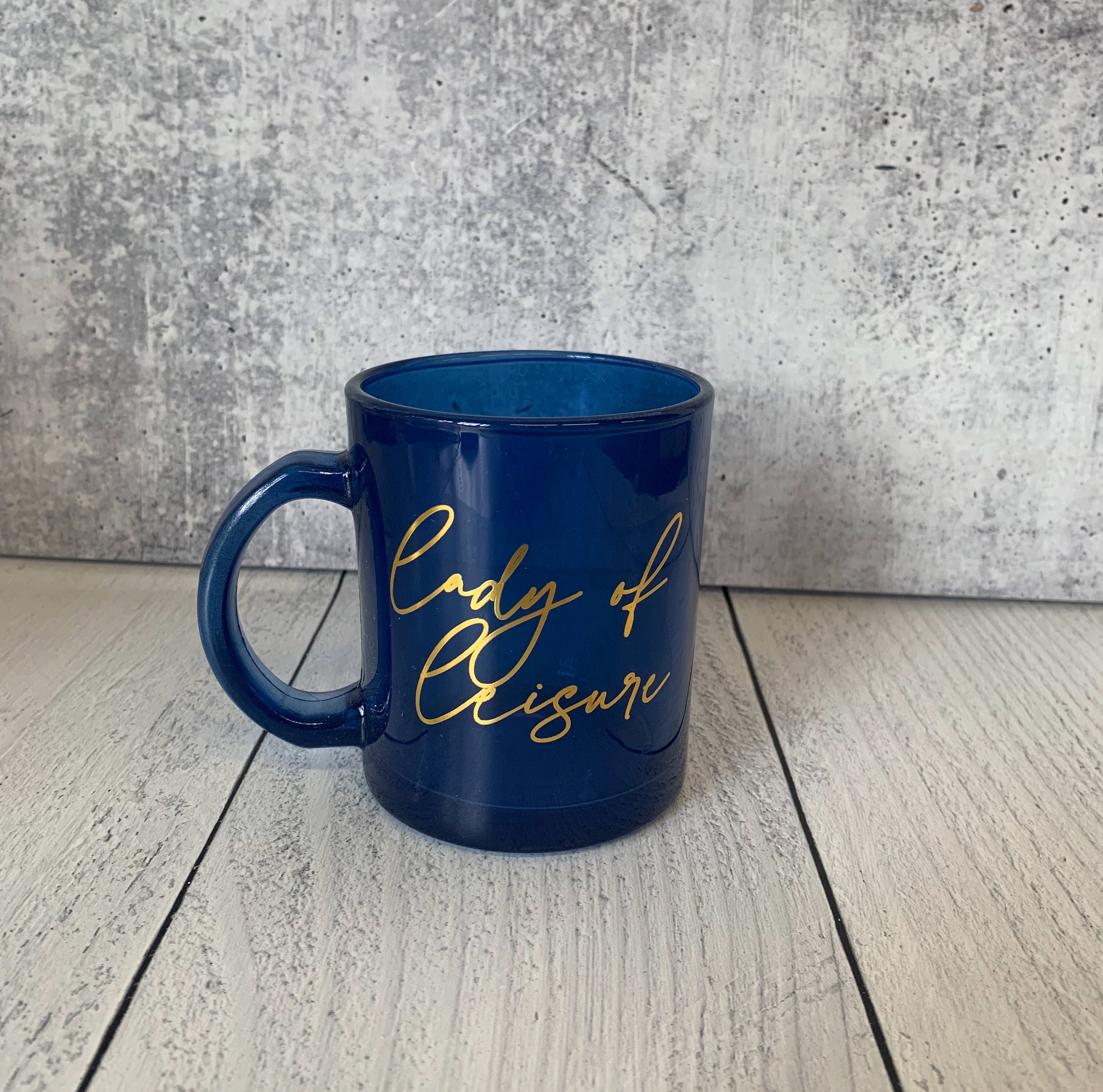 Lady of Leisure Single-Wall Glass Mug in dark blue tinted glass with gold lettering, elegantly designed for stylish sipping.