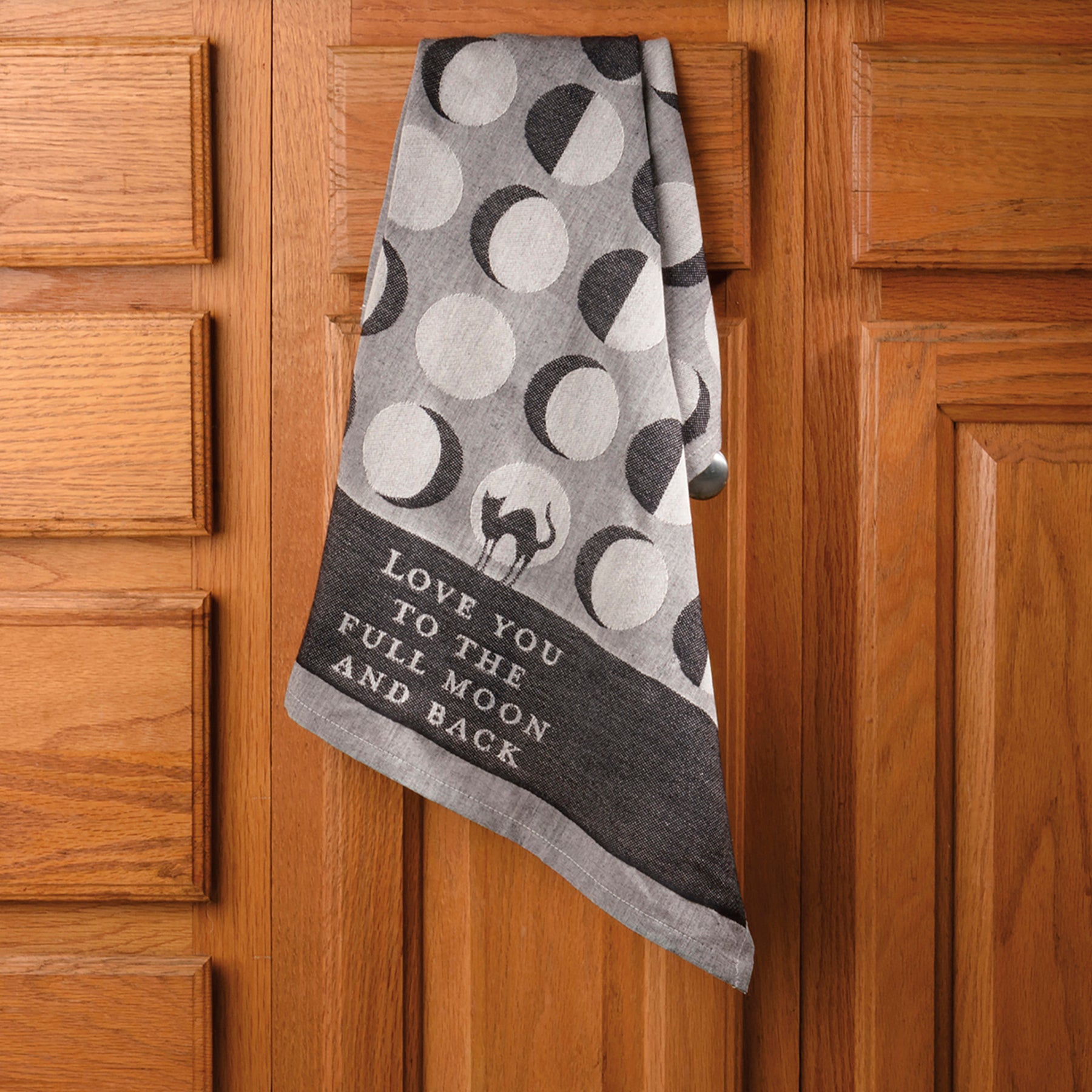 A jacquard woven kitchen towel featuring a cat silhouette and moon phase designs with the phrase 'Love You To The Full Moon And Back'.