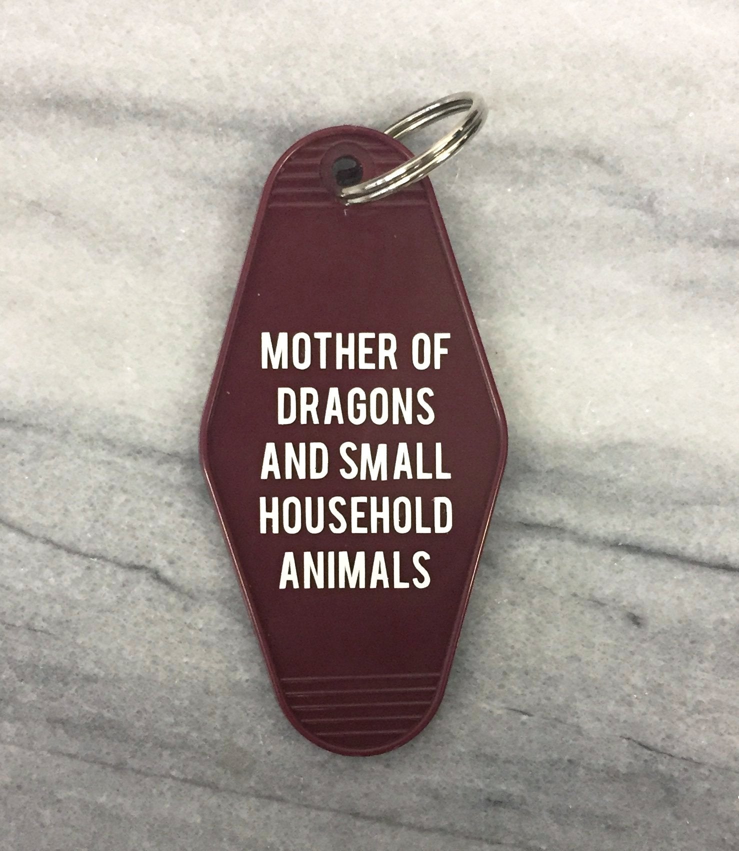 Dark red motel style keychain with white lettering reading 'MOTHER OF DRAGONS AND SMALL HOUSEHOLD ANIMALS', featuring a split ring.