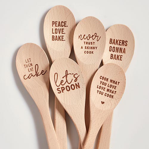 A wooden cooking spoon with the phrase 'Never Trust A Skinny Cook' engraved, placed in a stylish canvas gift bag.
