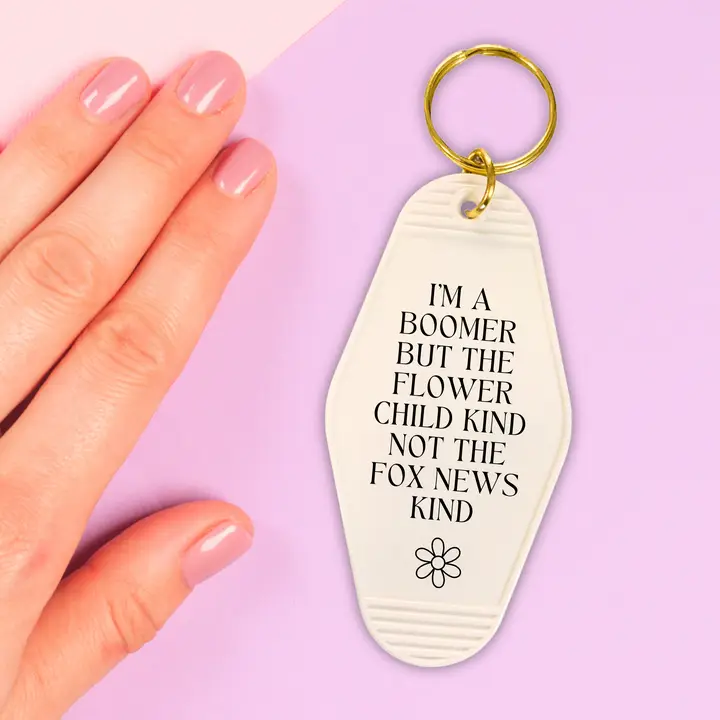 Black motel style keychain with the text 'I’M A BOOMER BUT THE FLOWER CHILD KIND NOT THE FOX NEWS KIND' and a split ring.