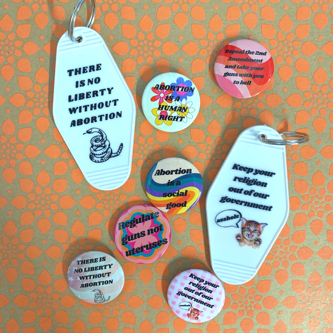 1.25-inch button featuring the phrase 'Regulate Guns Not Uteruses' with a colorful groovy flower design.