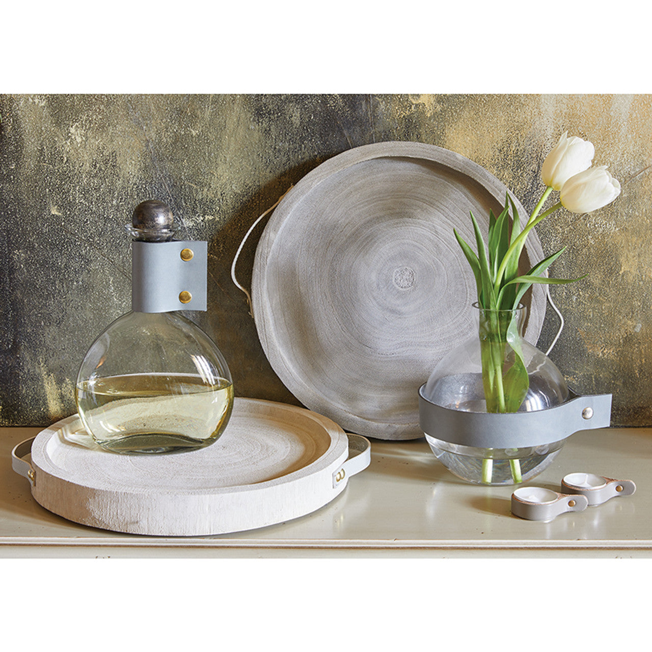 A 9-inch tall round glass vase with a grey leather cuff and brass fastener, elegantly showcasing flowers.