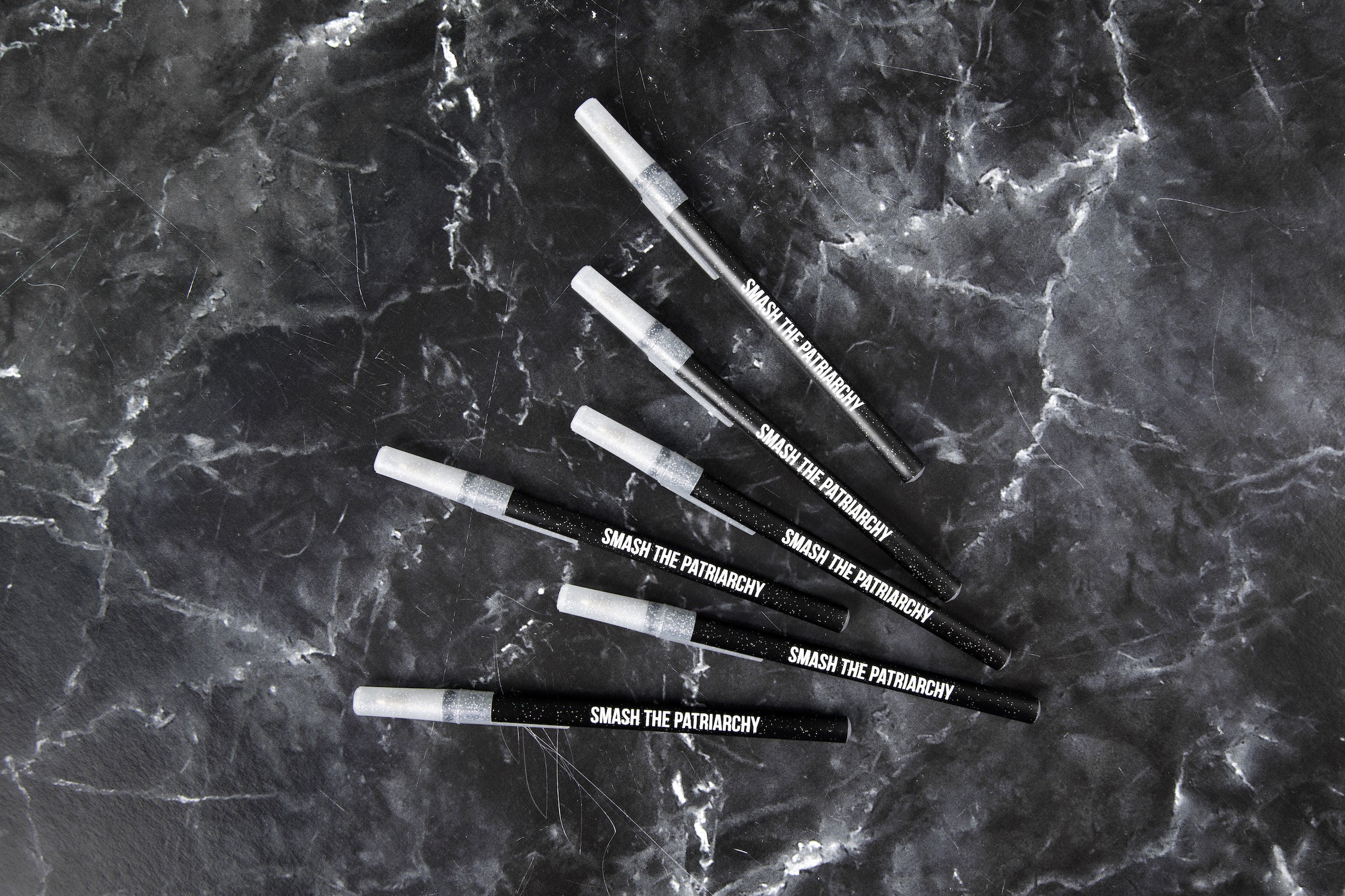 A pack of six Galaxy Sparkle pens with the phrase 'SMASH THE PATRIARCHY' printed on them, featuring a black sparkle body and clear sparkle cap.