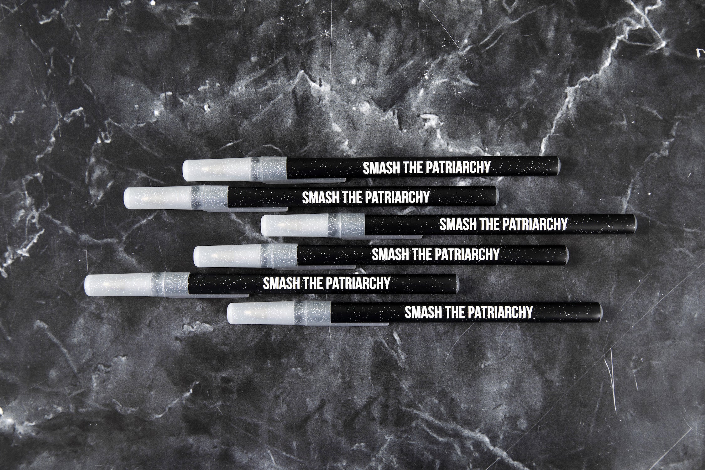 A pack of six Galaxy Sparkle pens with the phrase 'SMASH THE PATRIARCHY' printed on them, featuring a black sparkle body and clear sparkle cap.