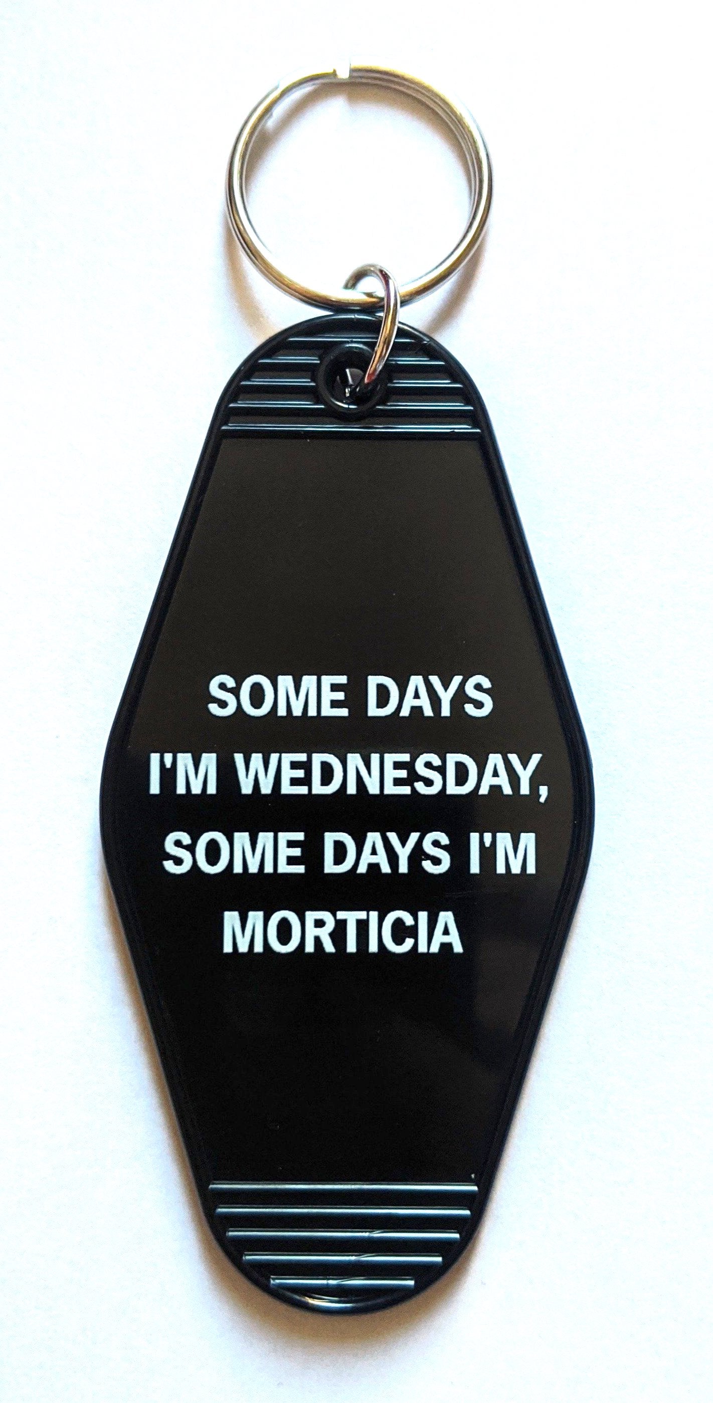 Black motel-style keychain with white lettering reading 'Some Days I'm Wednesday, Some Days I'm Morticia', featuring a split ring.