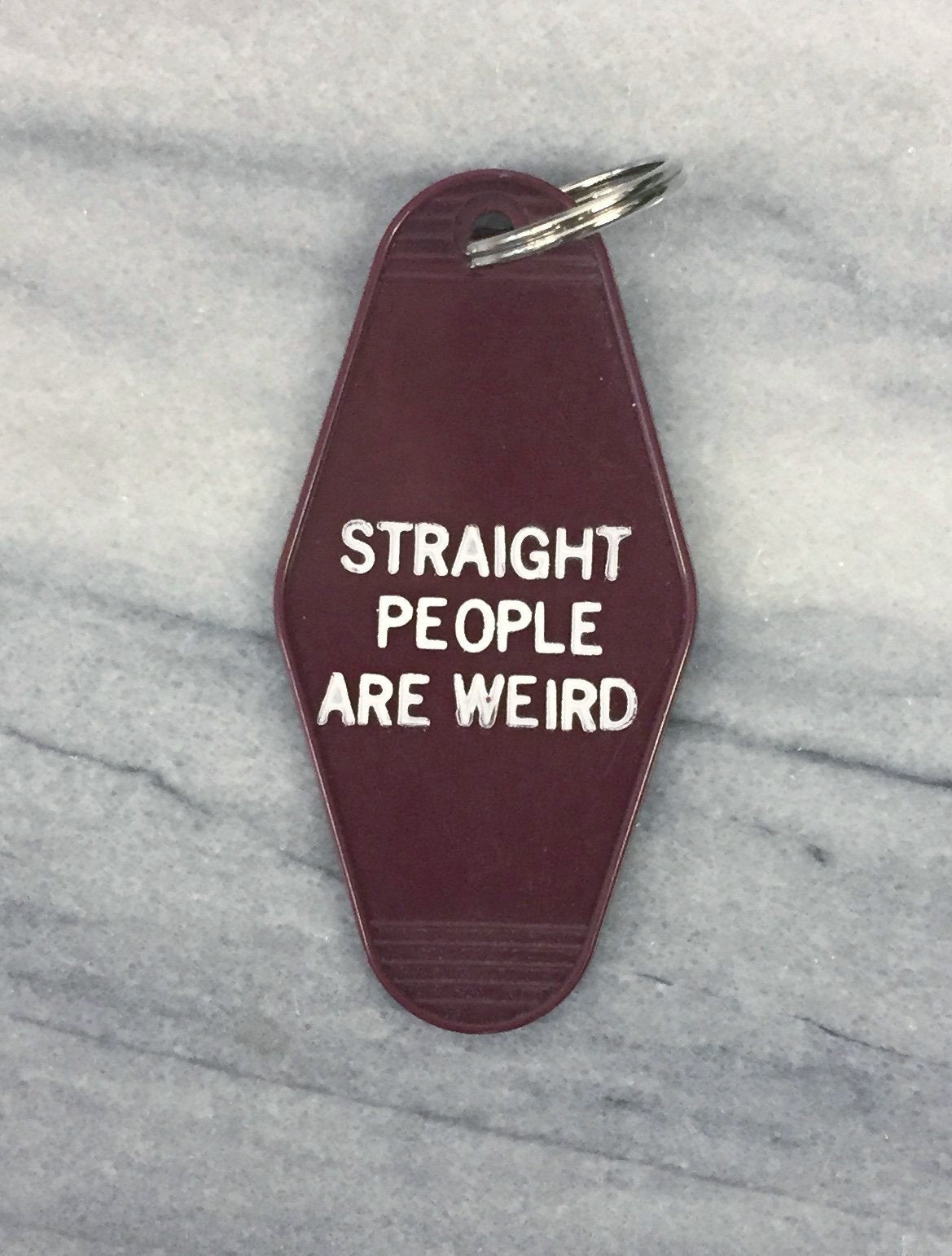 Dark red motel-style keychain with white text reading 'STRAIGHT PEOPLE ARE WEIRD', featuring a split ring and hand-stamped design.